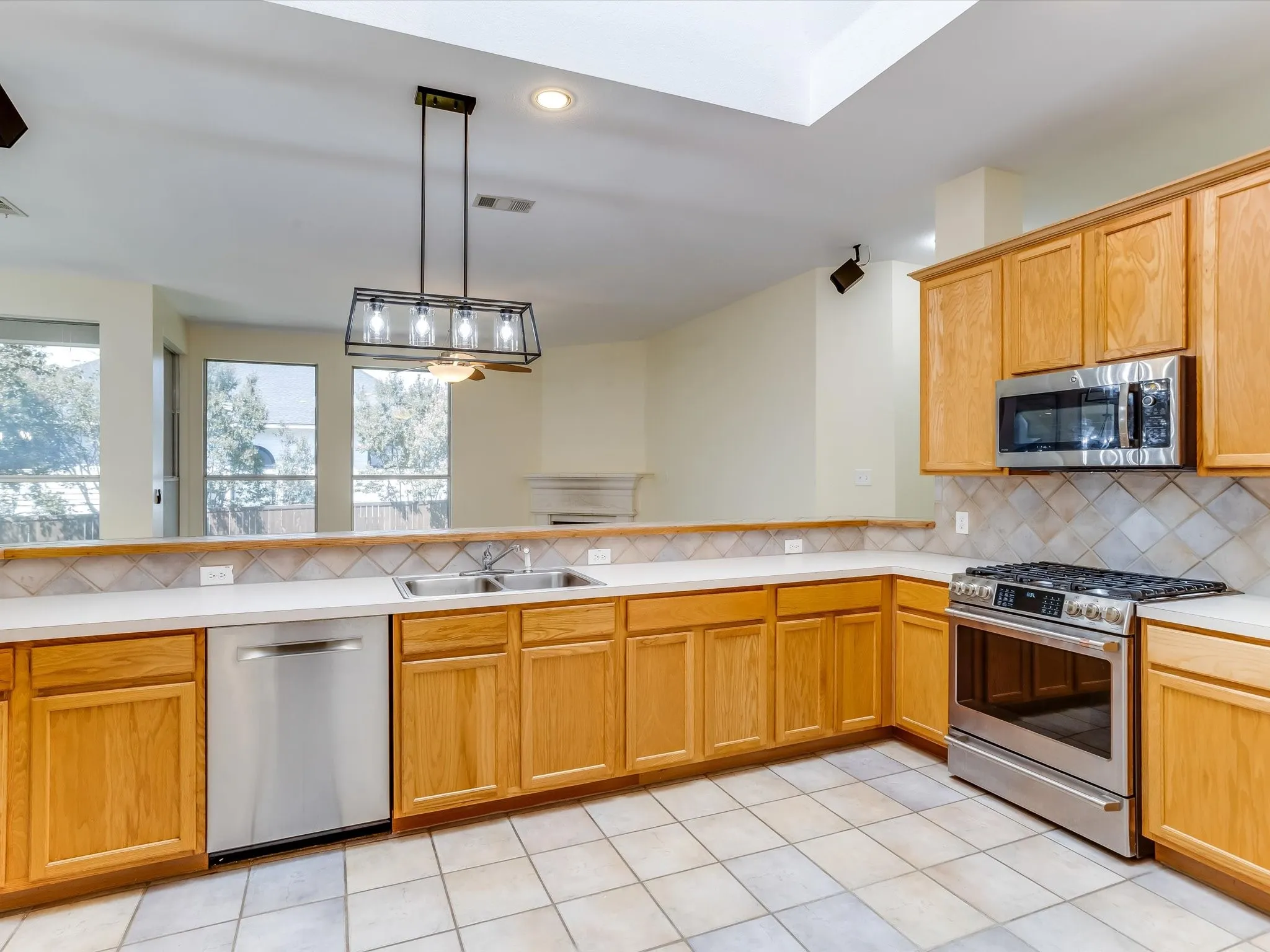 Spacious kitchen featuring warm wood cabinetry, stainless steel gas range and microwave, white dishwasher, tile flooring, and marble countertops with herringbone backsplash
