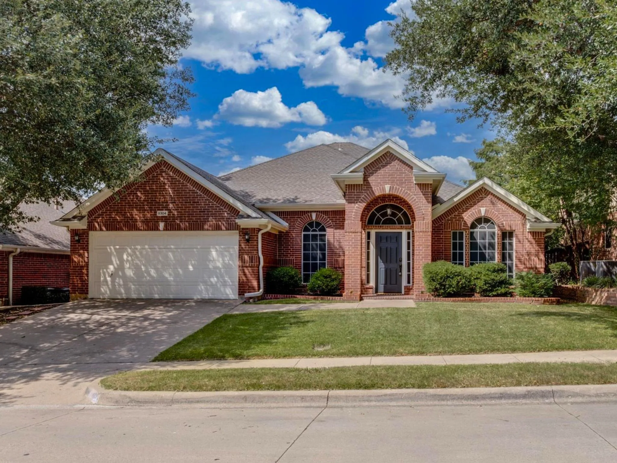 Brick facade residence featuring a two-car garage, arched entryways, and a manicured lawn