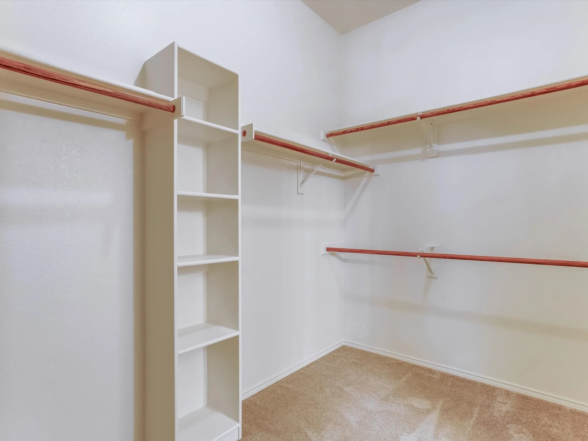 Walk-in closet featuring built-in shelving with five open compartments, dual wooden hanging rods with brass hardware, and cork composite flooring