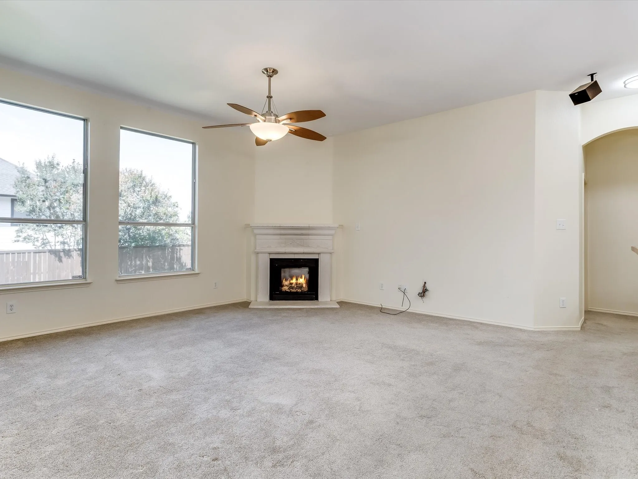 Living area featuring a corner fireplace with a white mantel, beige carpeting, and multiple windows