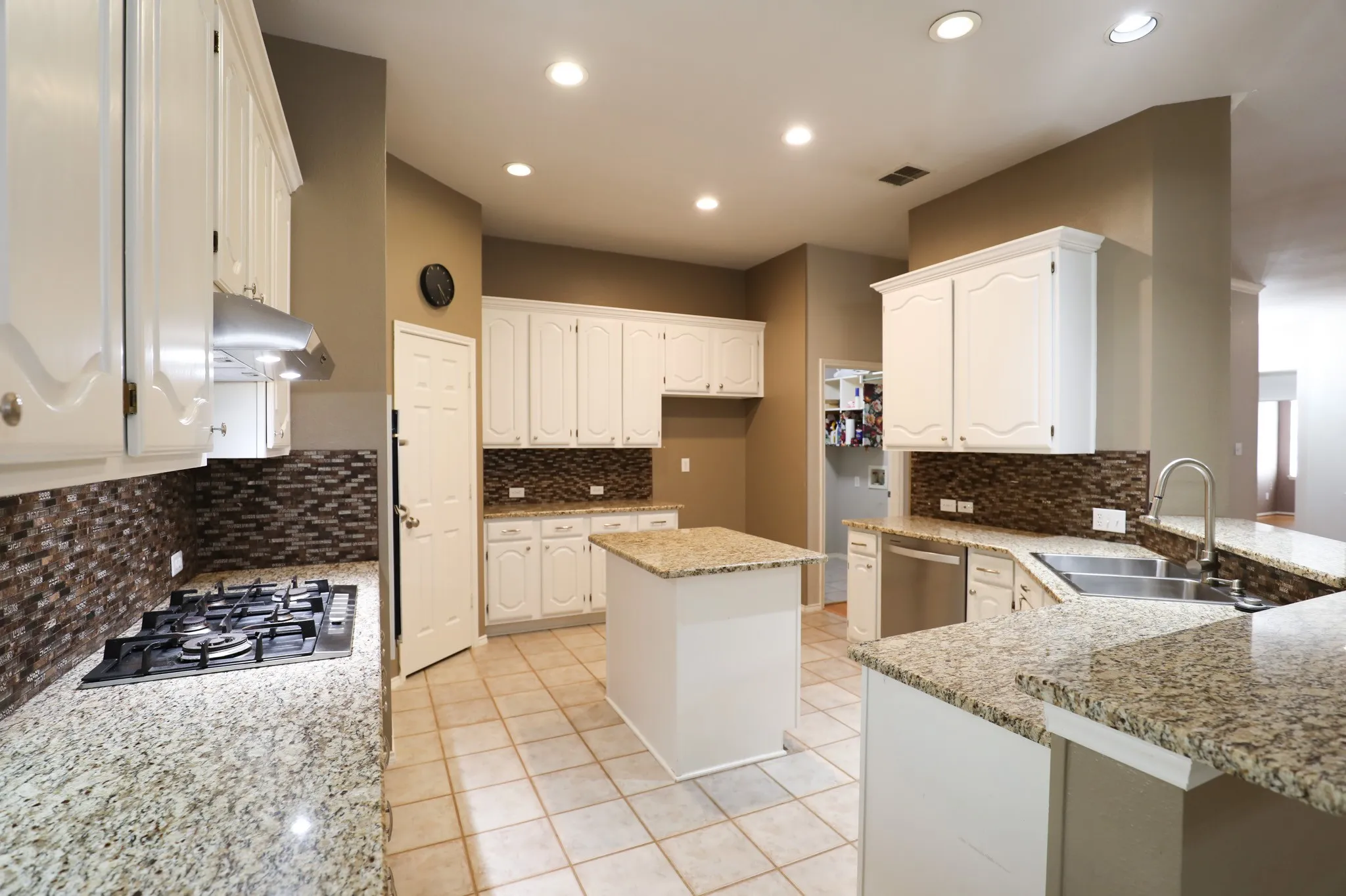 White cabinetry, granite countertops, tile flooring, mosaic tile backsplash, and a central island