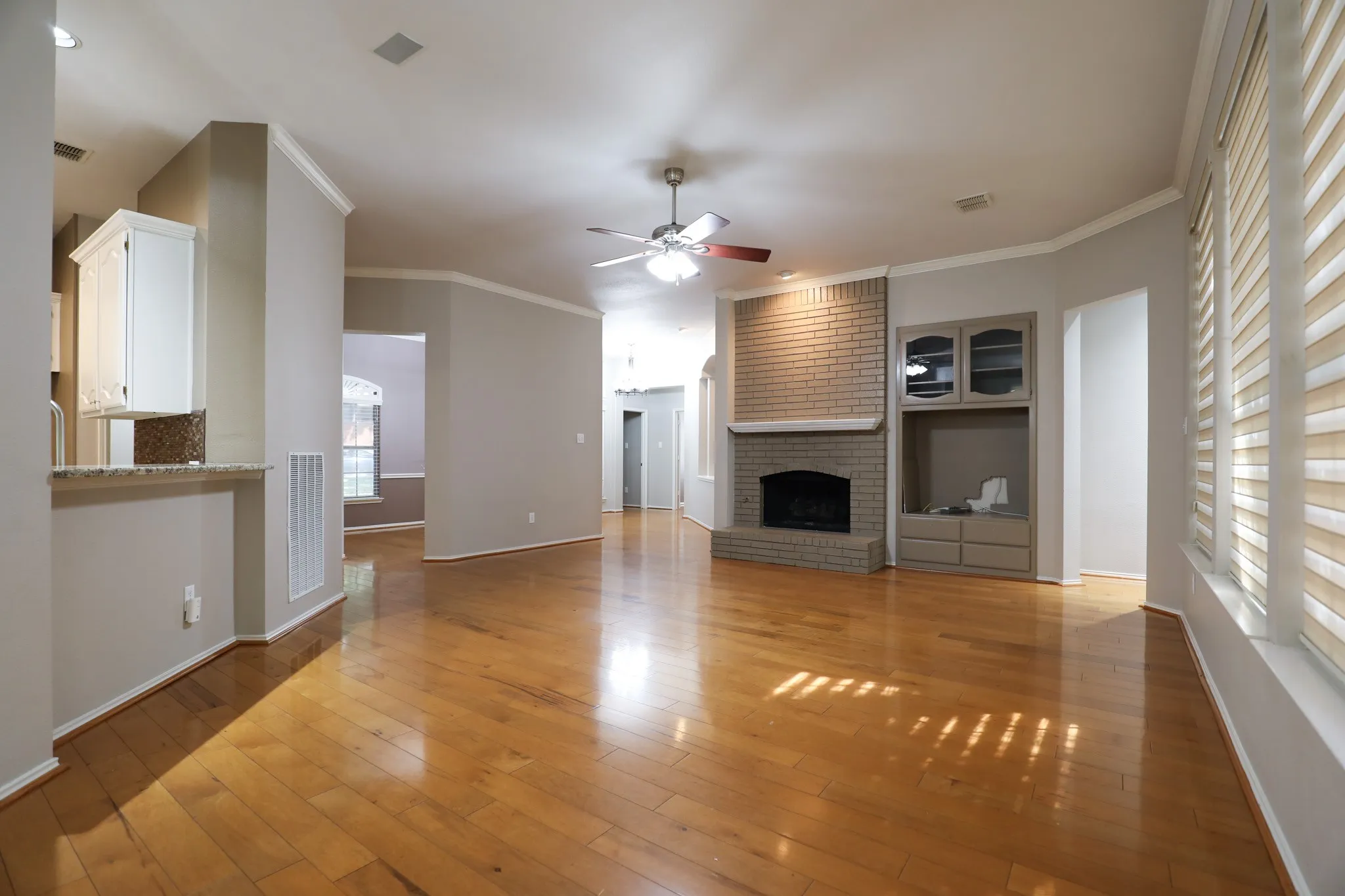 Wood-finish flooring throughout, brick fireplace with mantel, built-in cabinetry, and a ceiling fan
