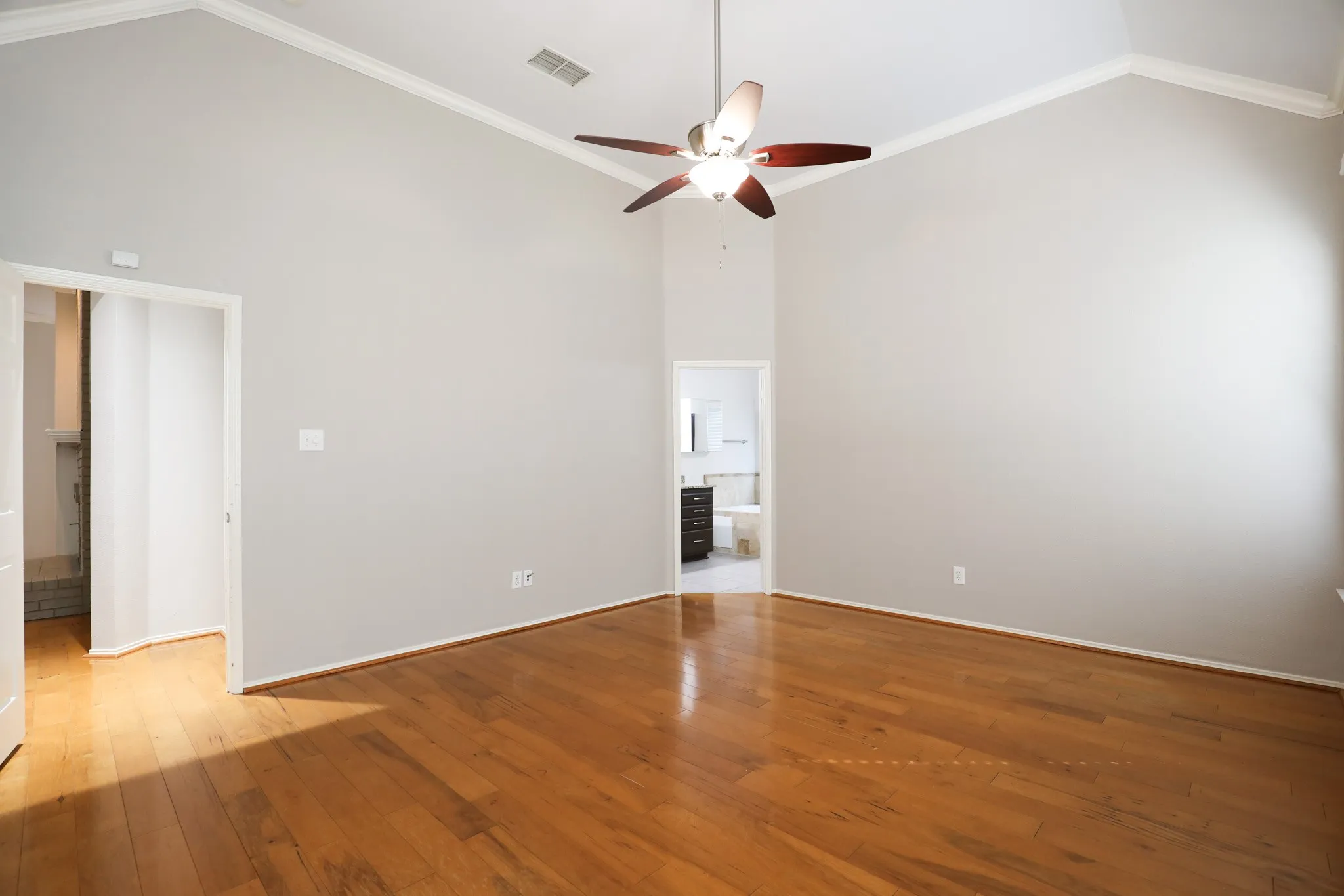 High vaulted ceilings with crown molding, wood-finish flooring, and a ceiling fan with light fixture