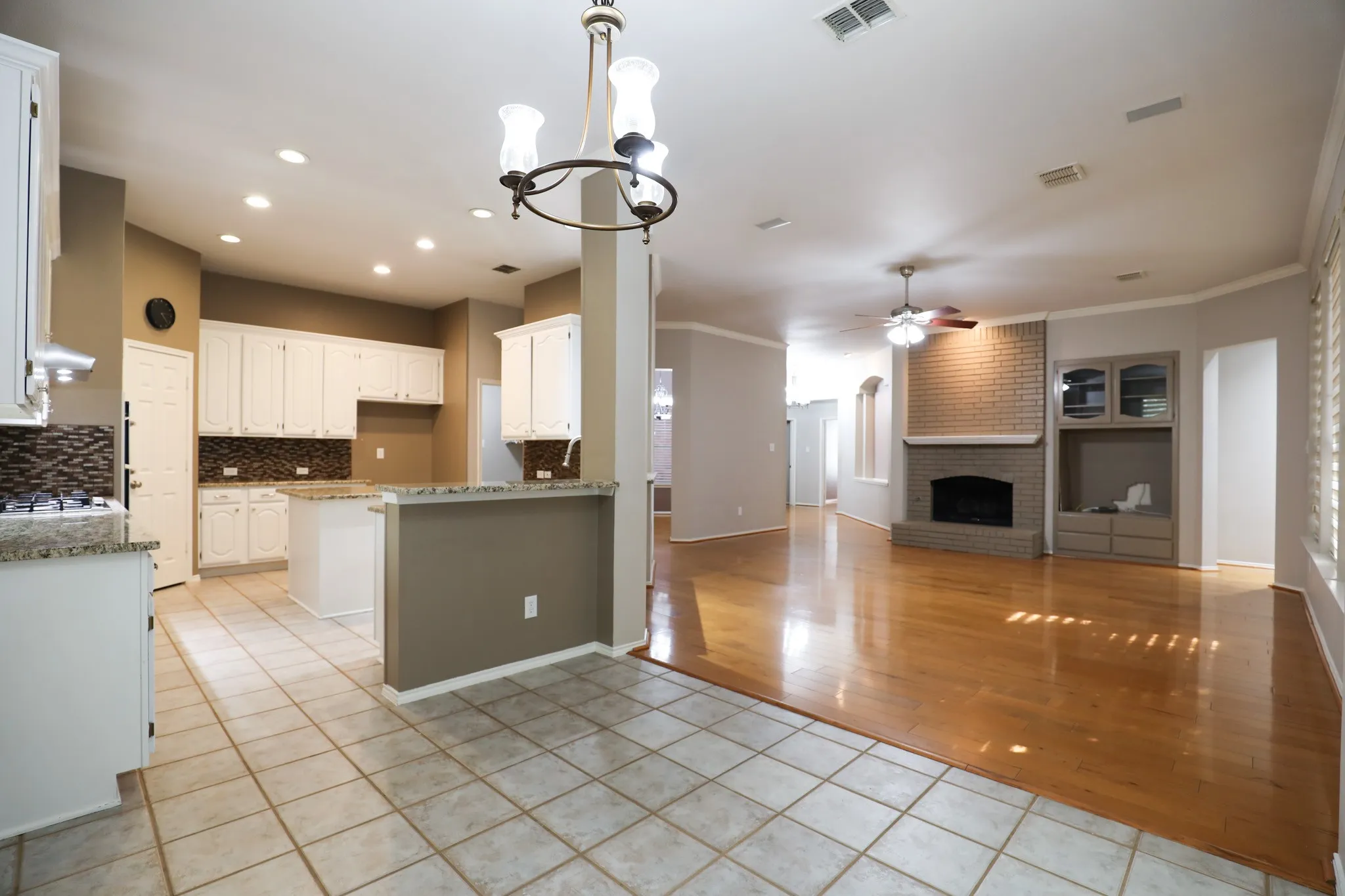 Expansive open-concept living area featuring wood-finish flooring, a brick fireplace with a hearth, and built-in shelving