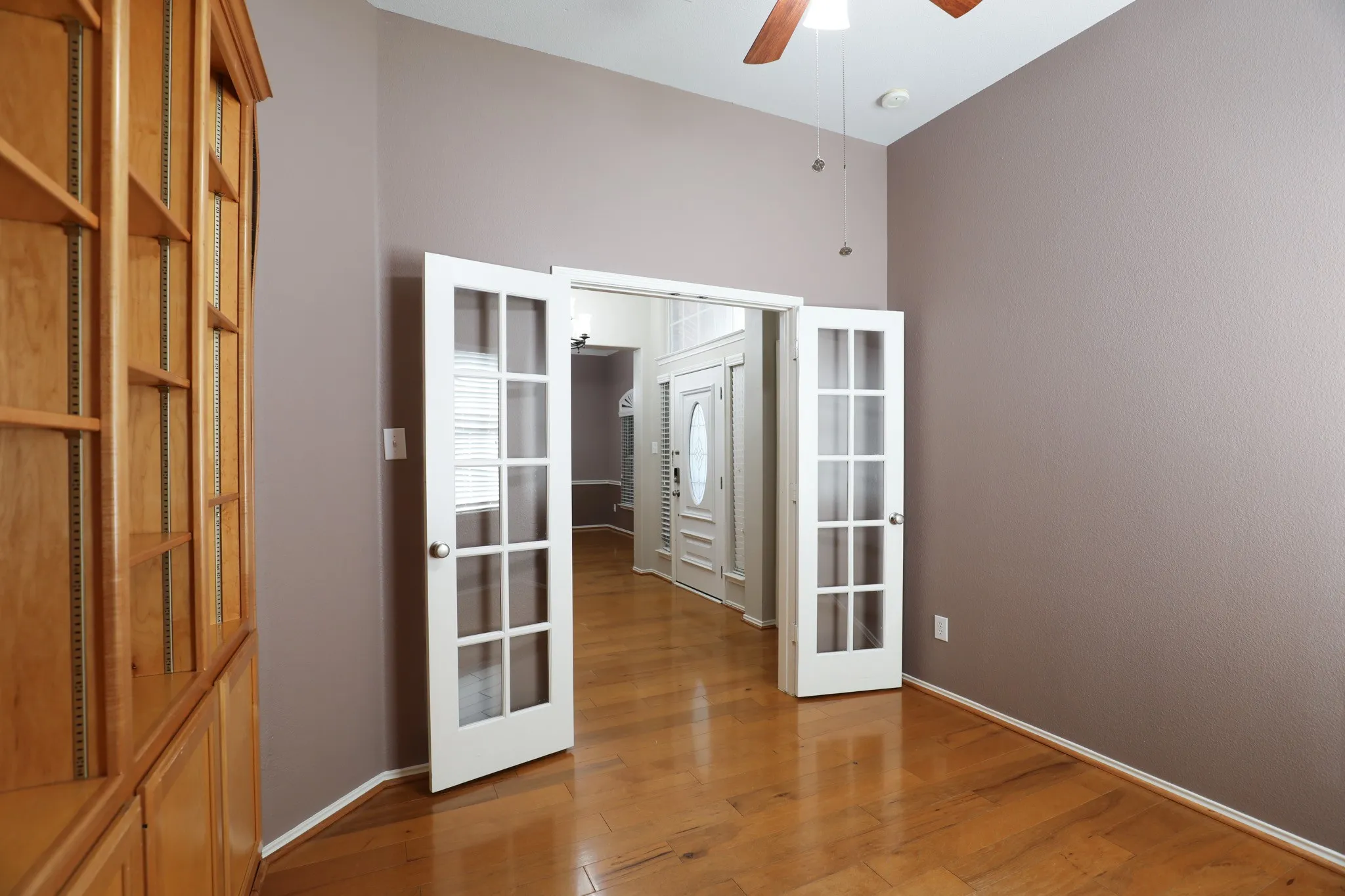 Wood-finish flooring, built-in shelving, vaulted ceiling, ceiling fan, and French doors
