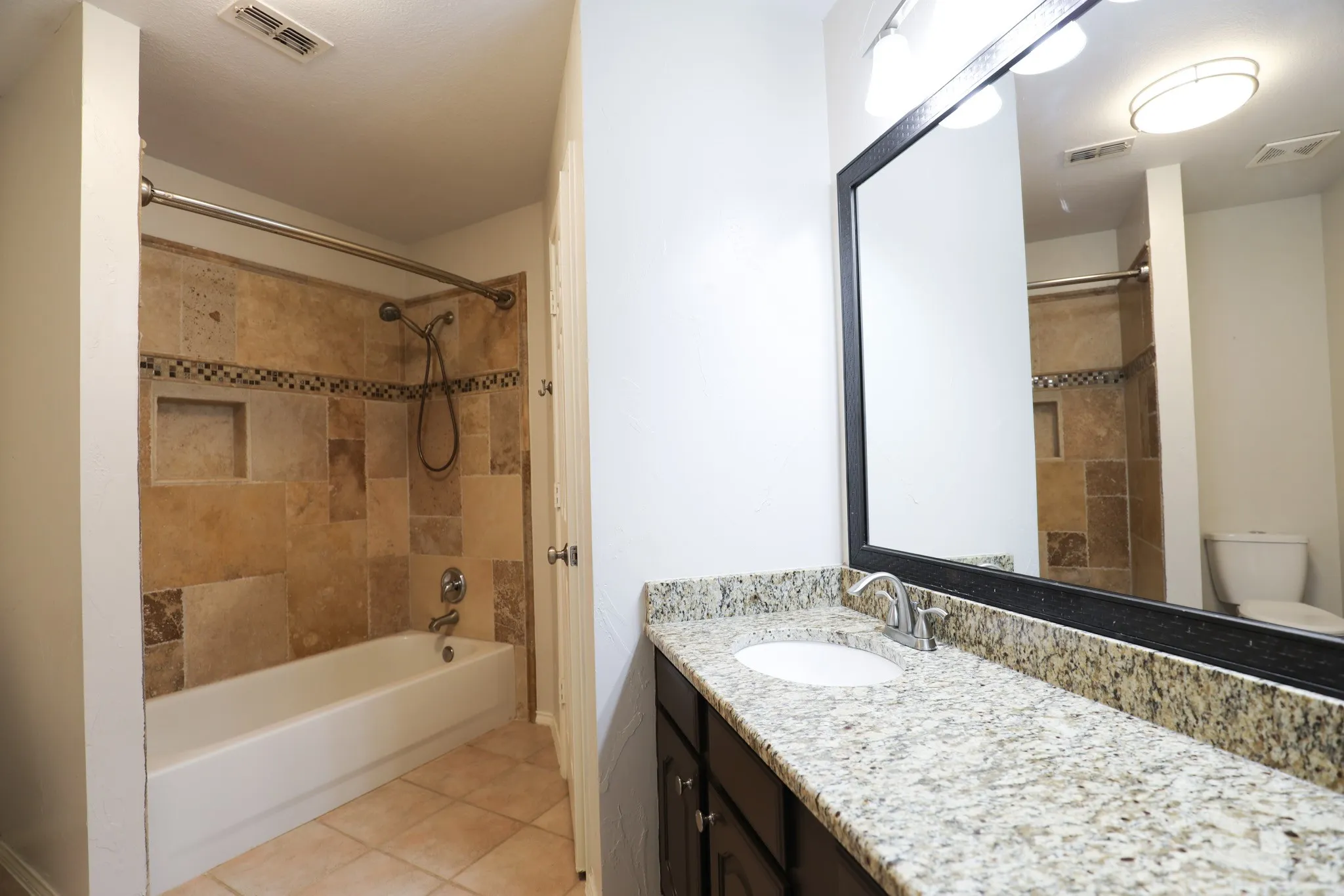 Bathroom featuring a vanity with a light-toned stone countertop, integrated sink, and a large framed mirror