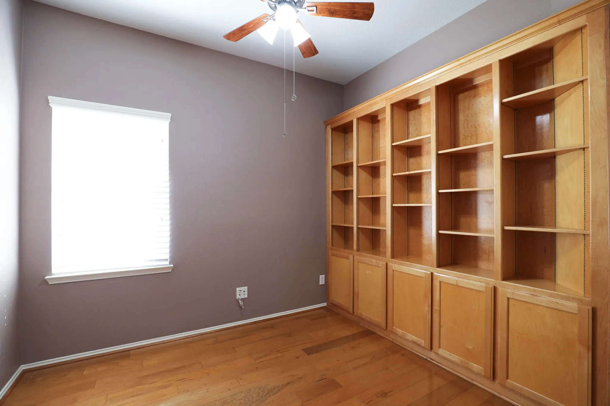 Built-in wood-finish cabinetry and shelving, wood-finish flooring, and a ceiling fan