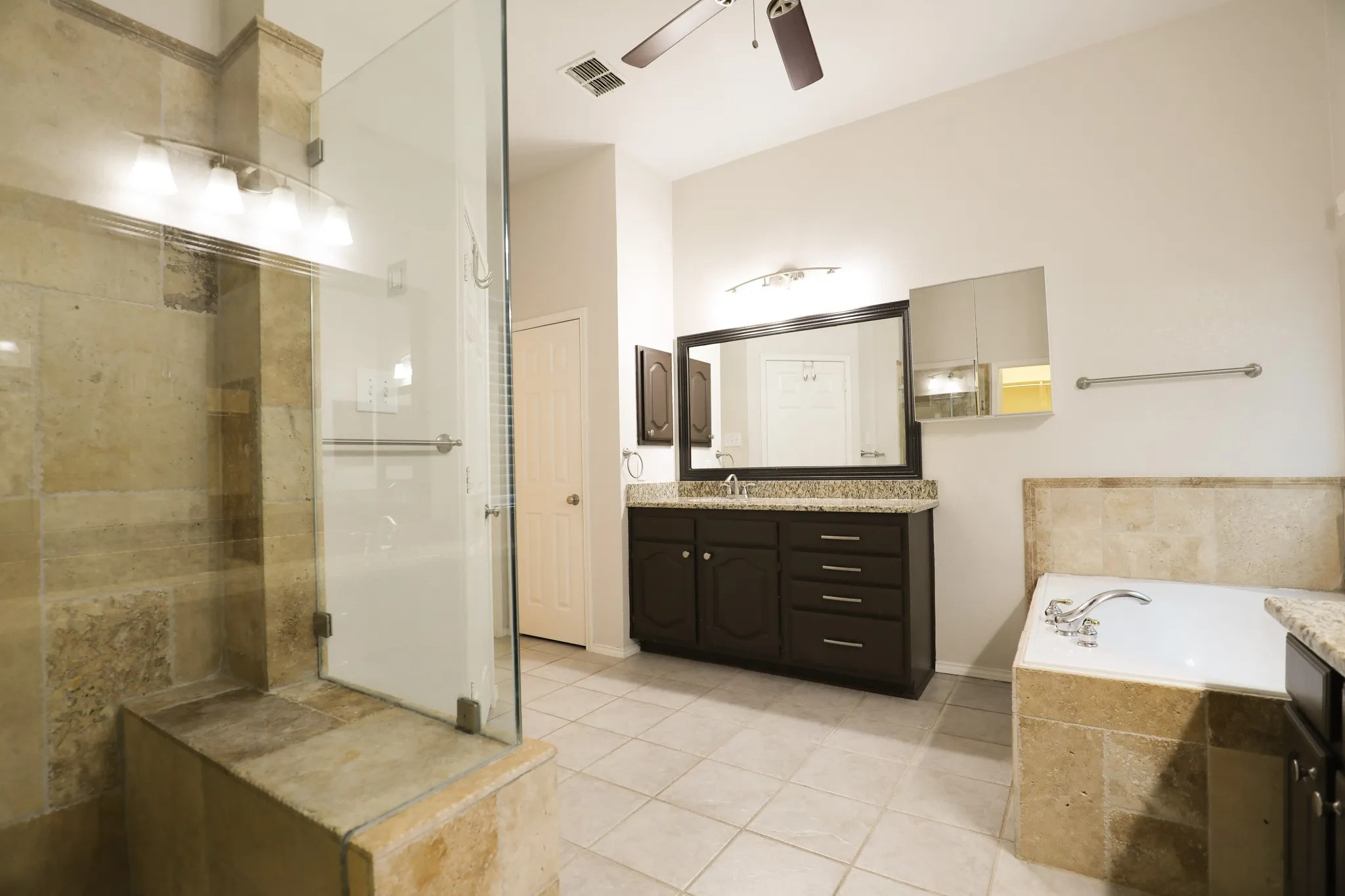 Glass-enclosed shower with a built-in bench, stone tile surround, and an integrated lighting fixture