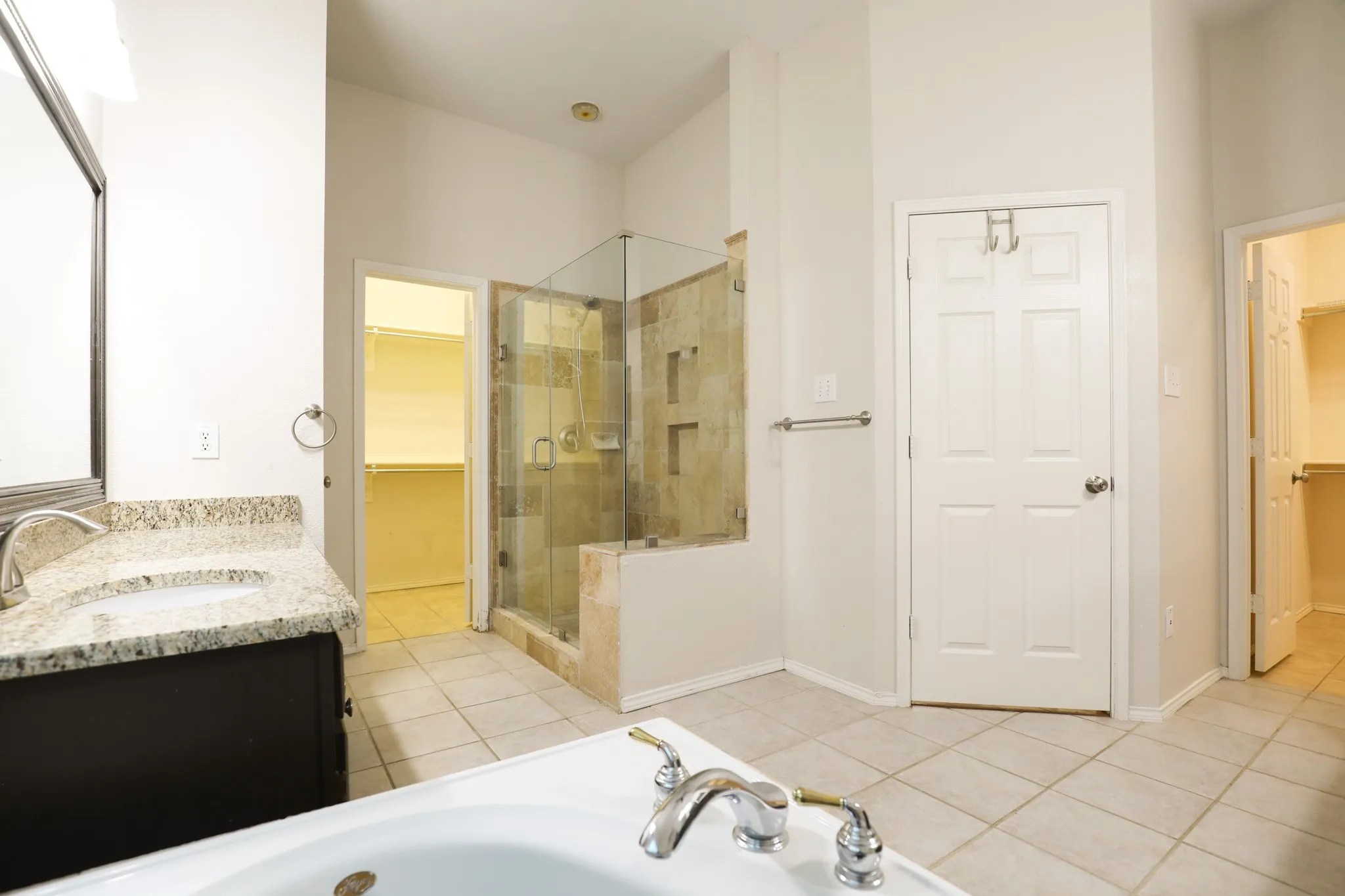 Dual vanity with granite countertop, frameless glass shower enclosure, separate soaking tub, and tile flooring