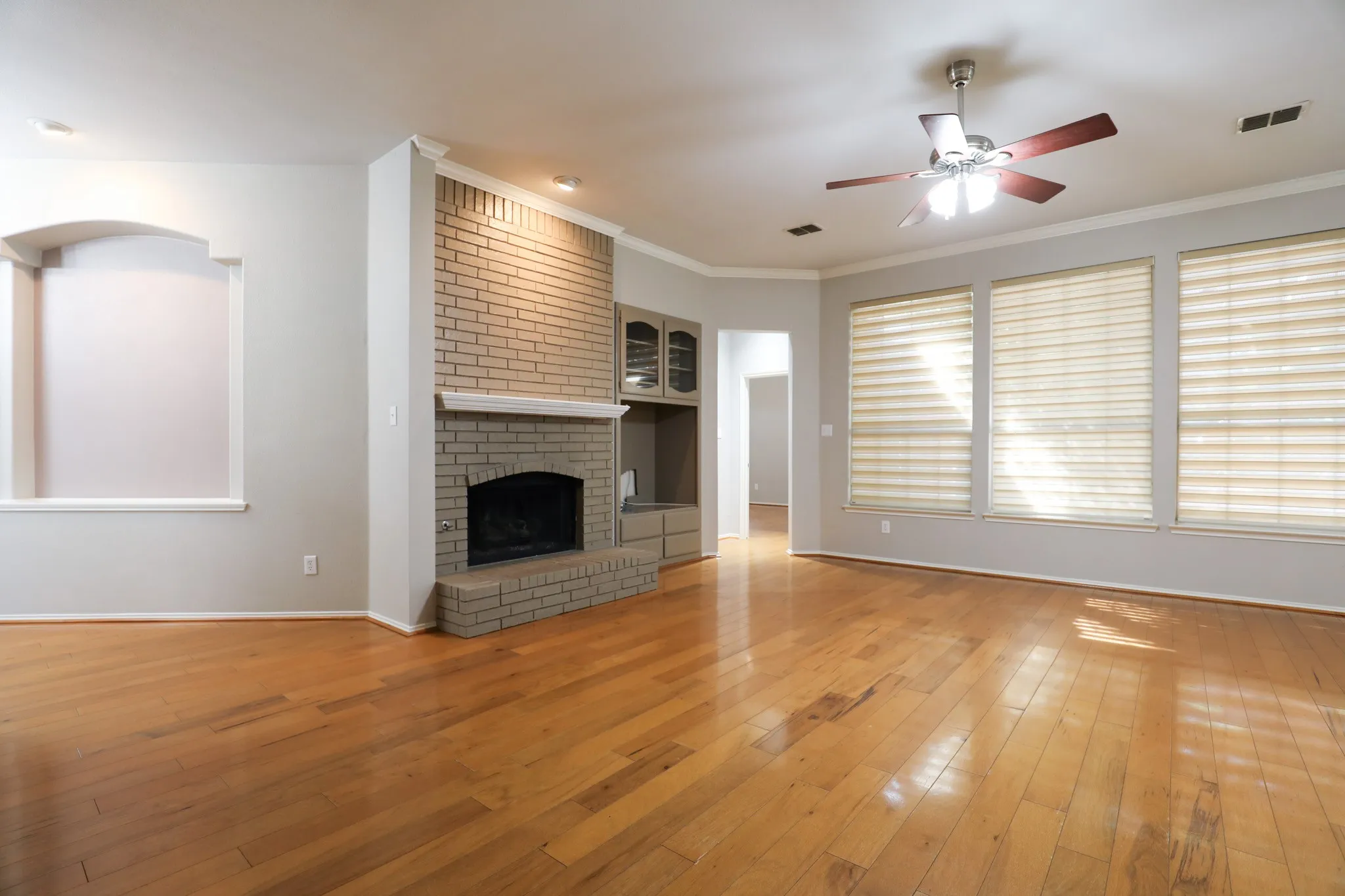 Wood-finish flooring throughout, brick fireplace with a mantle, built-in cabinetry, multiple windows, and a ceiling fan