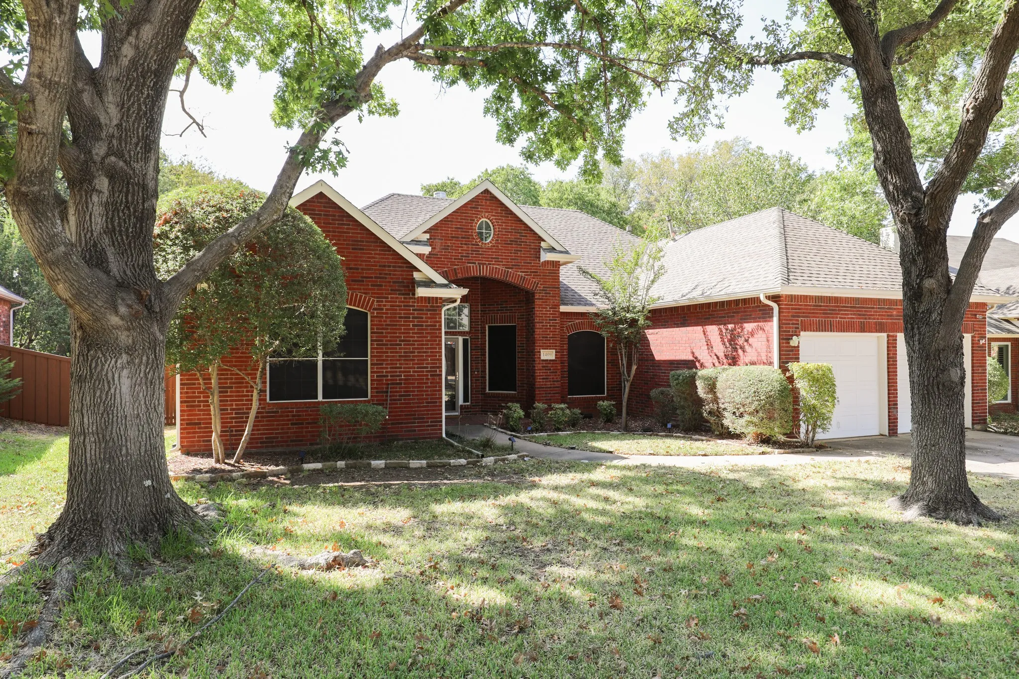 Brick exterior with arched entryway, attached garage, and mature trees