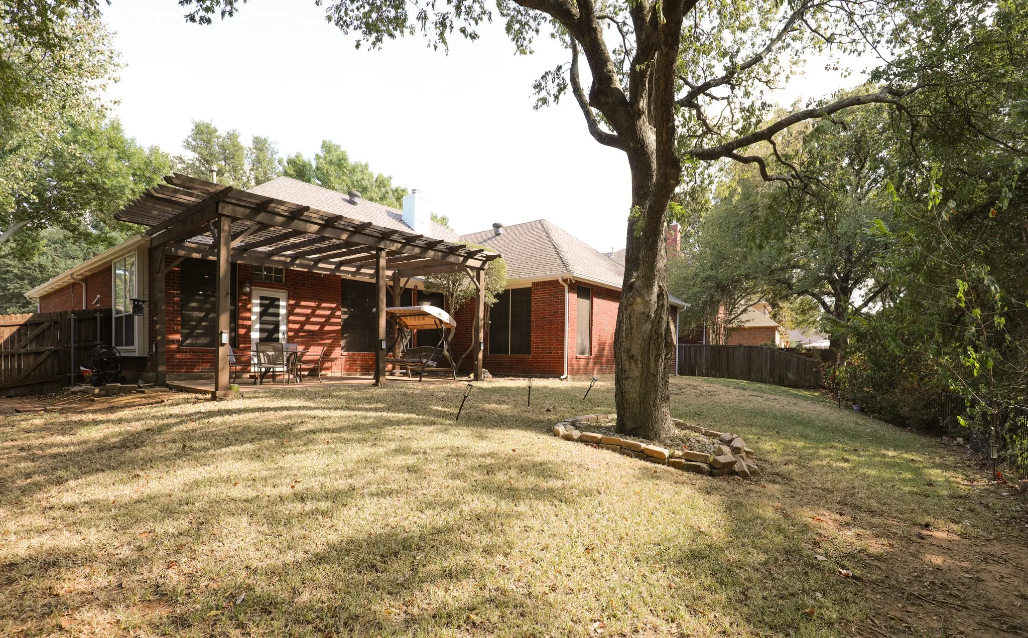 Expansive backyard featuring a wood pergola, red brick exterior, mature trees, and a privacy fence