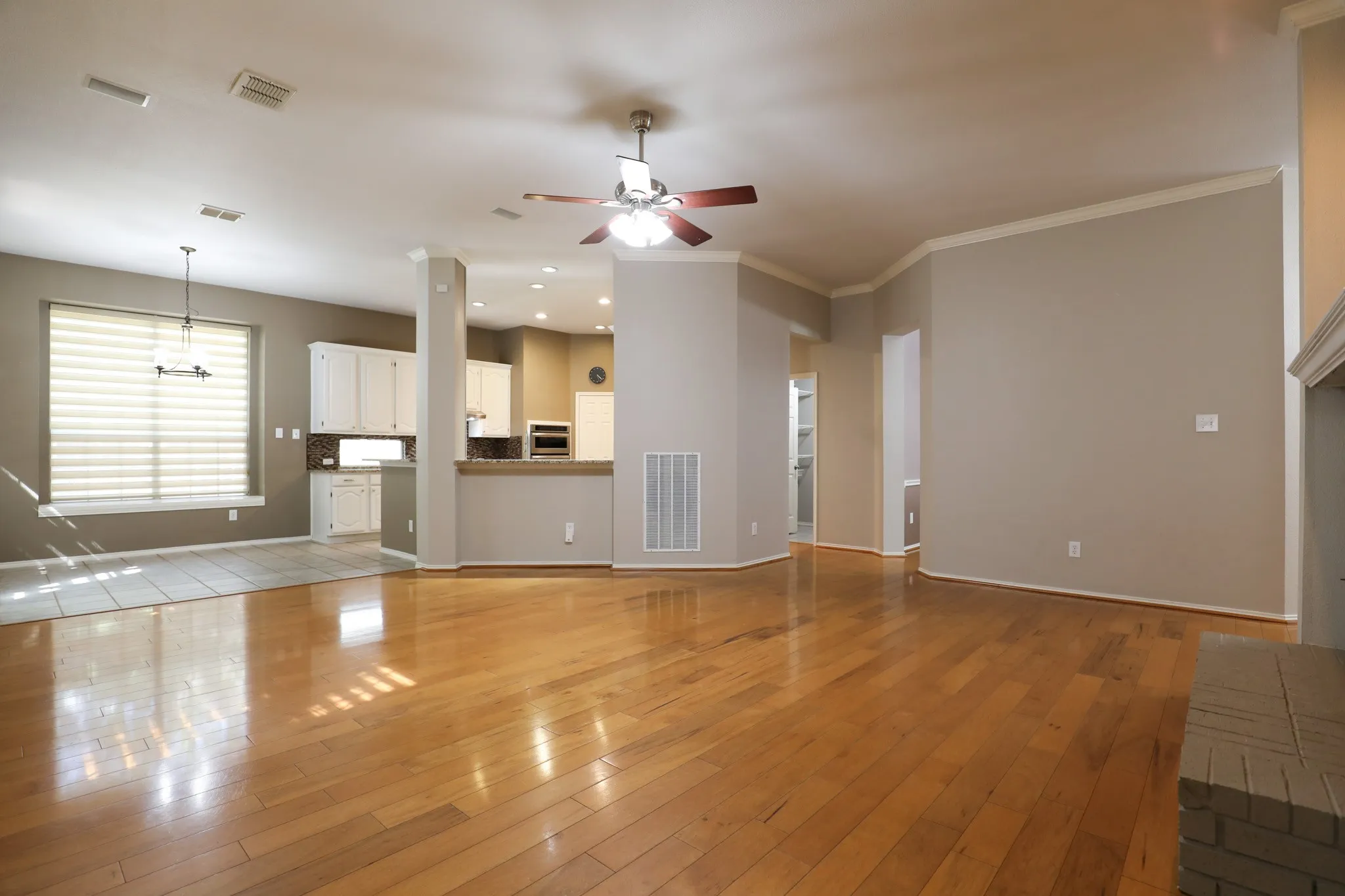 Hardwood flooring, crown molding, ceiling fan, white cabinetry, and a brick fireplace surround