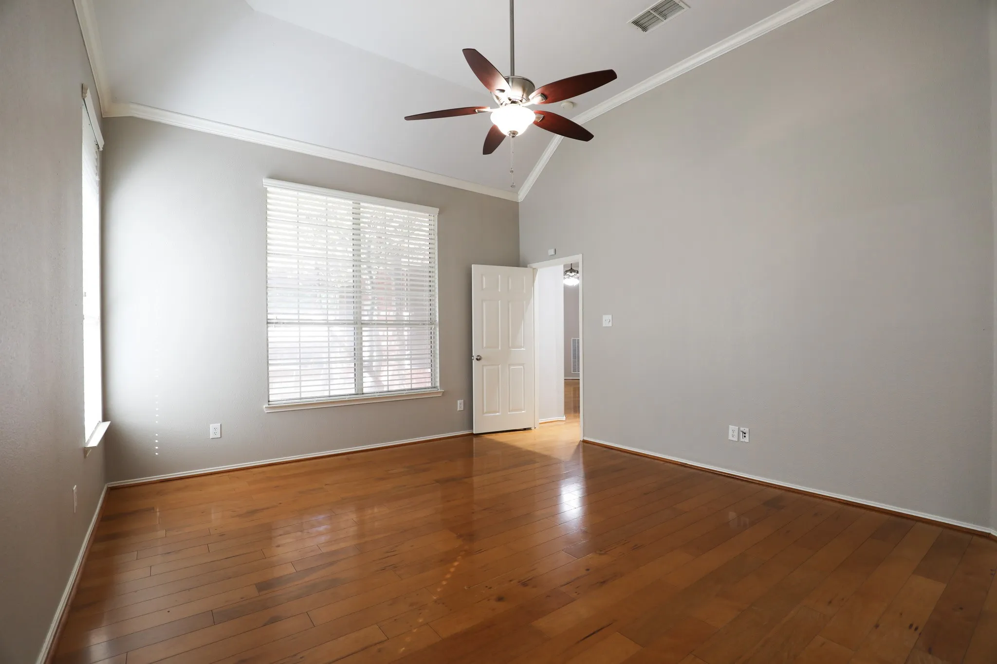 Wood-finish flooring, vaulted ceiling, ceiling fan with integrated lighting, multiple windows, and white trim throughout