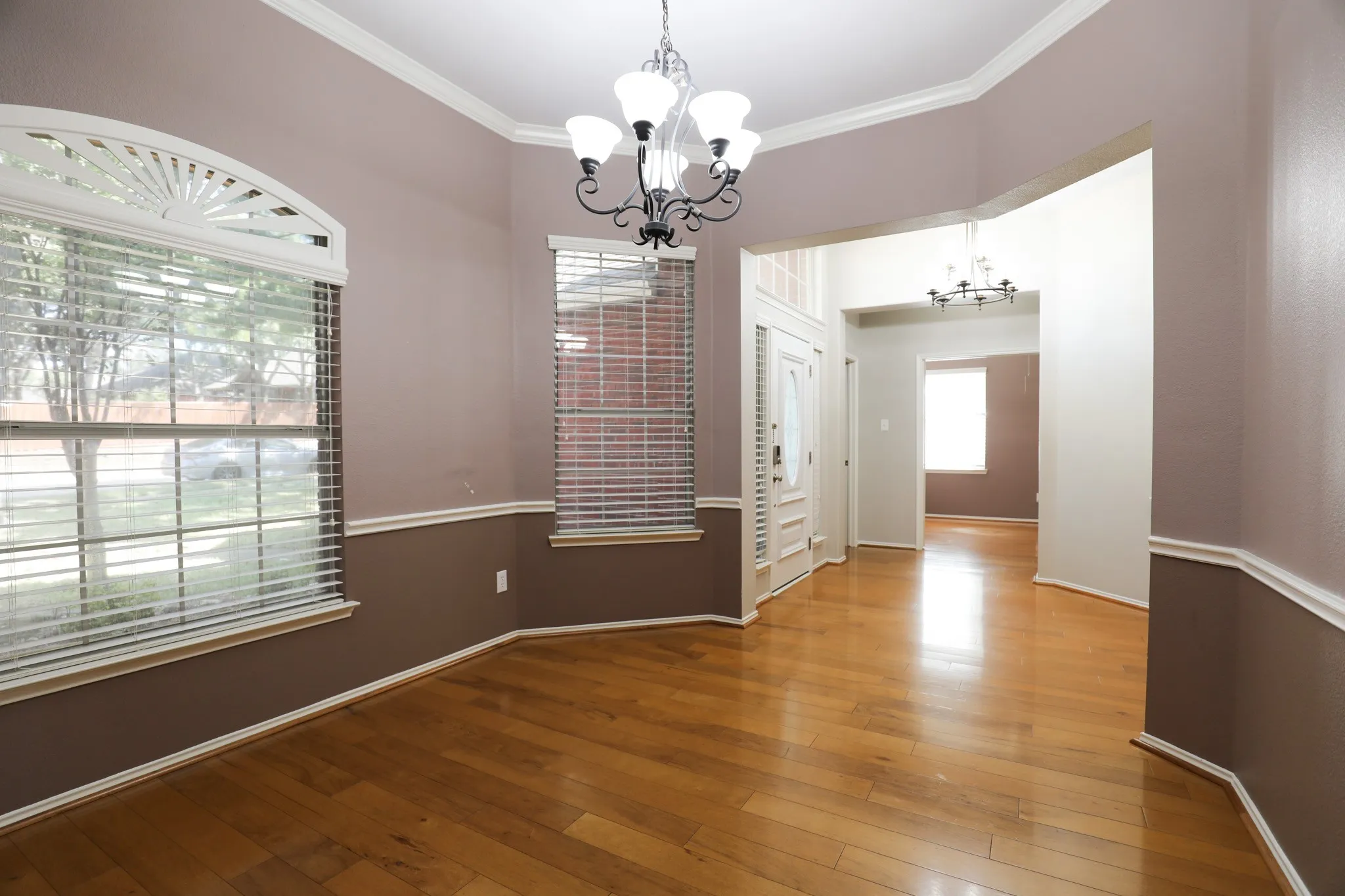 Wood-finish flooring, decorative chandelier, arched window with a fanlight transom, two-tone wall treatment, and crown molding