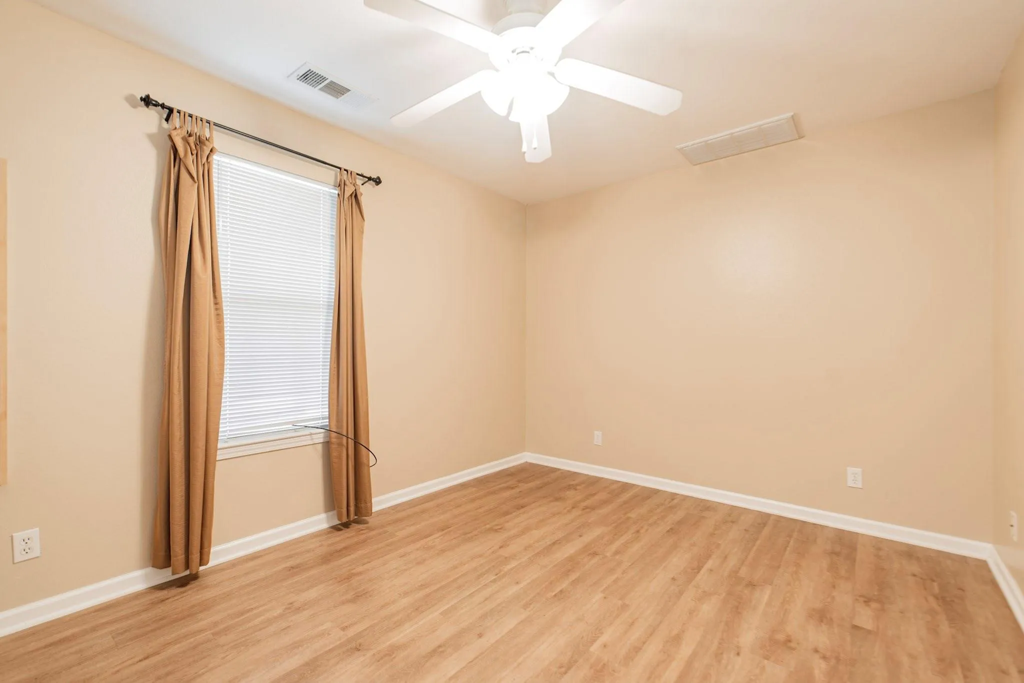 Spacious room featuring light wood-finish flooring, a ceiling fan with integrated lighting, and a window with blinds