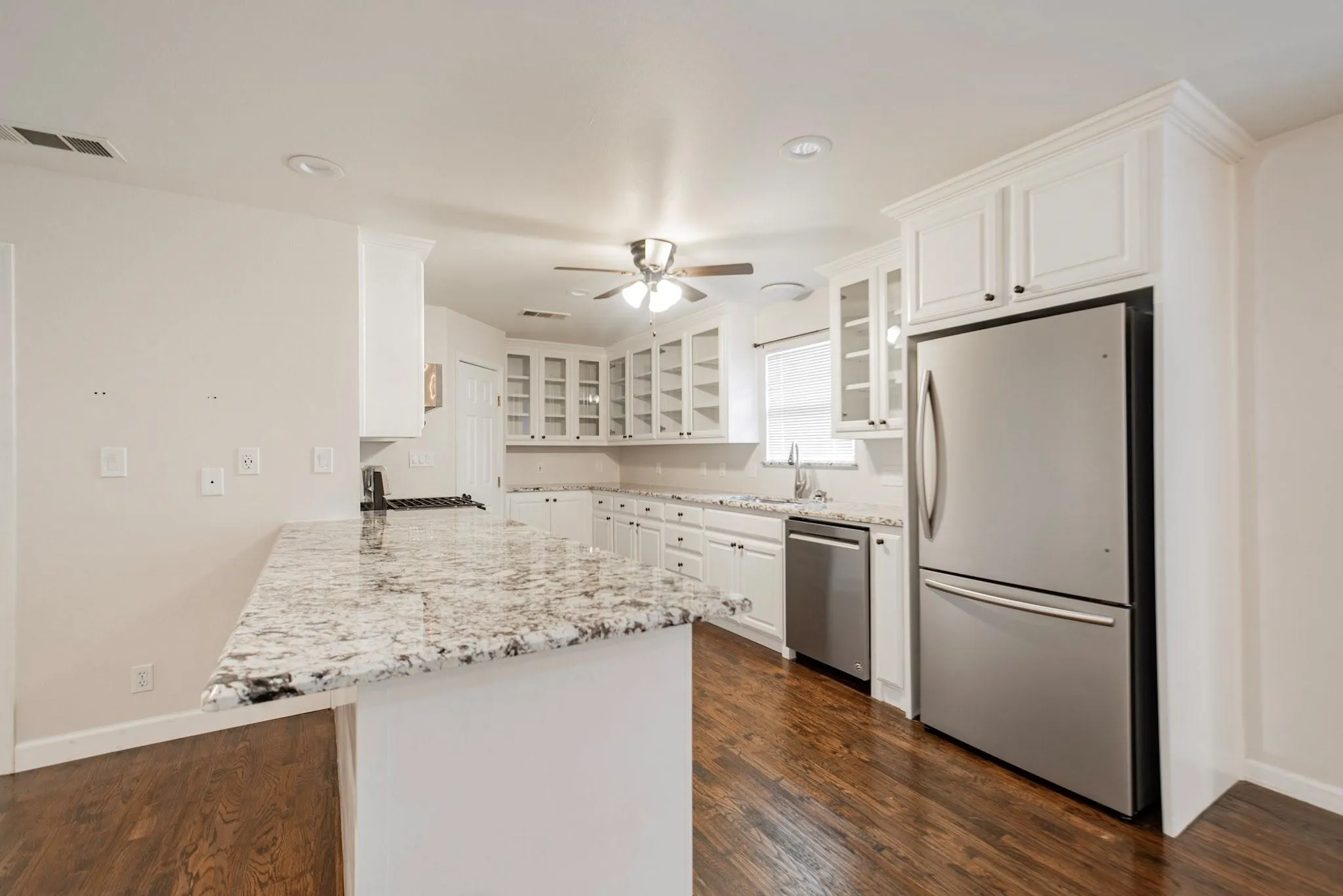 Kitchen featuring wood-finish flooring, white cabinetry with crown molding, stainless steel appliances, speckled countertops, and recessed lighting