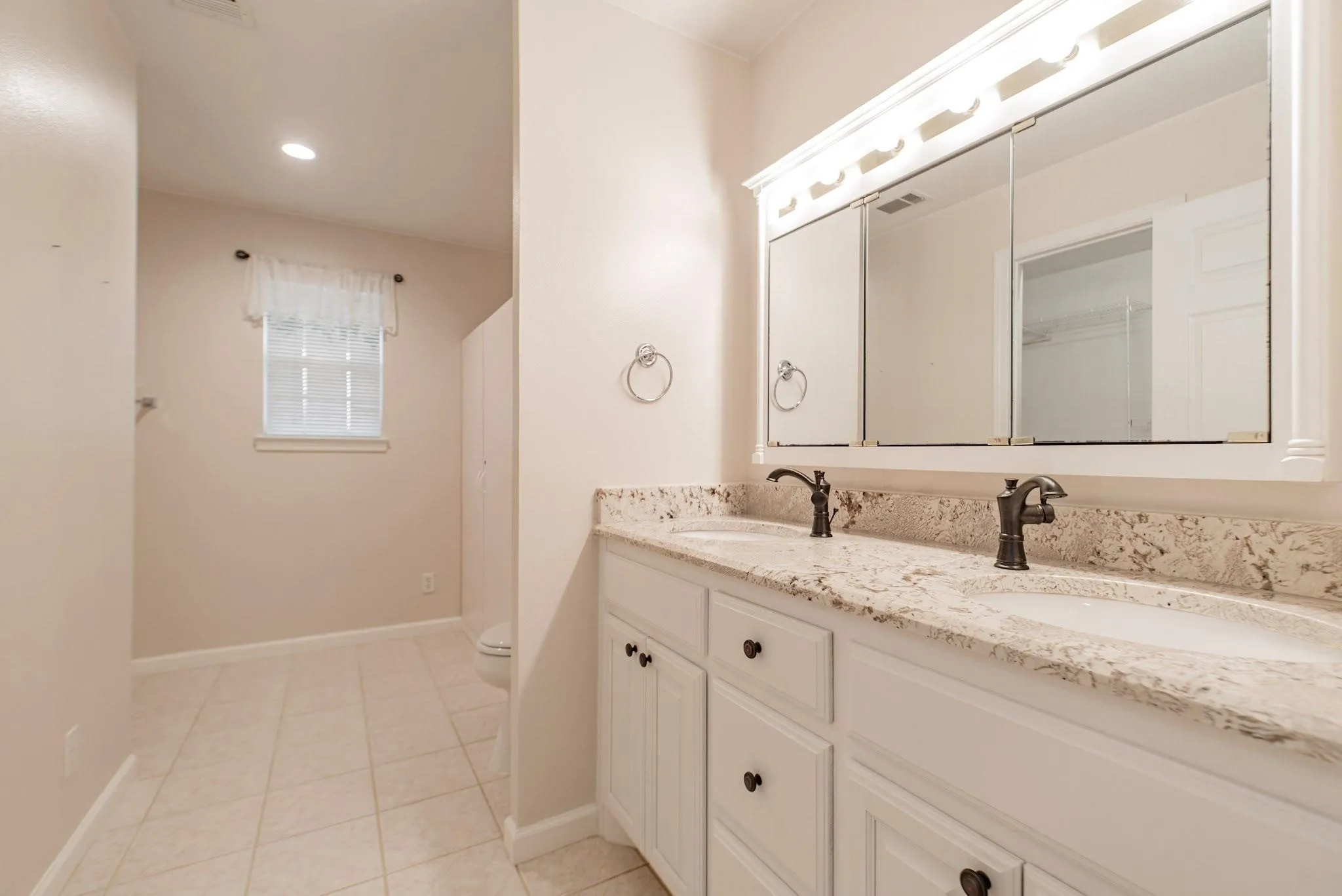 Dual vanity with white cabinetry, bronze-finish fixtures, and a light-toned countertop