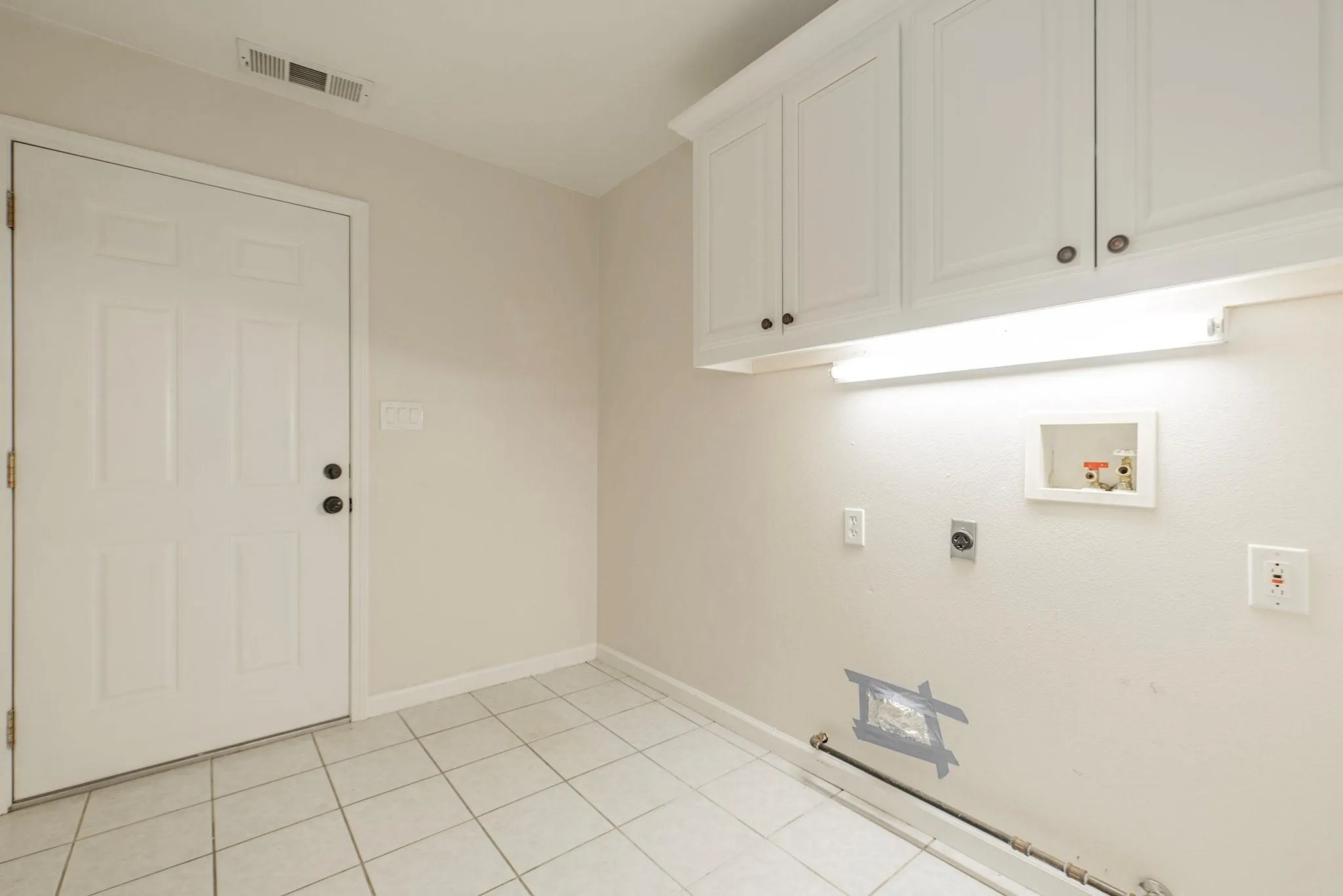 Utility area featuring light-toned tile flooring, overhead cabinetry, and a bright fluorescent fixture
