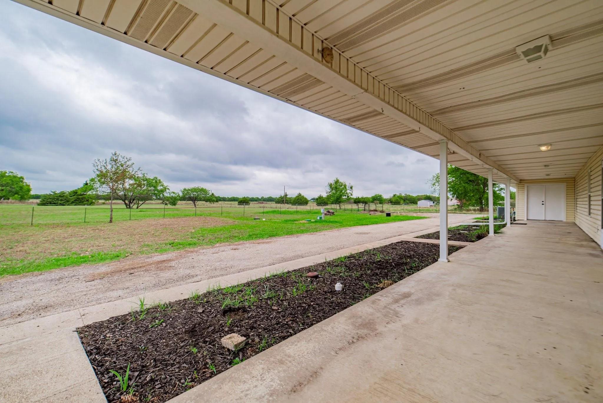 Expansive covered front porch with a concrete slab, supporting pillars, and overhead lighting