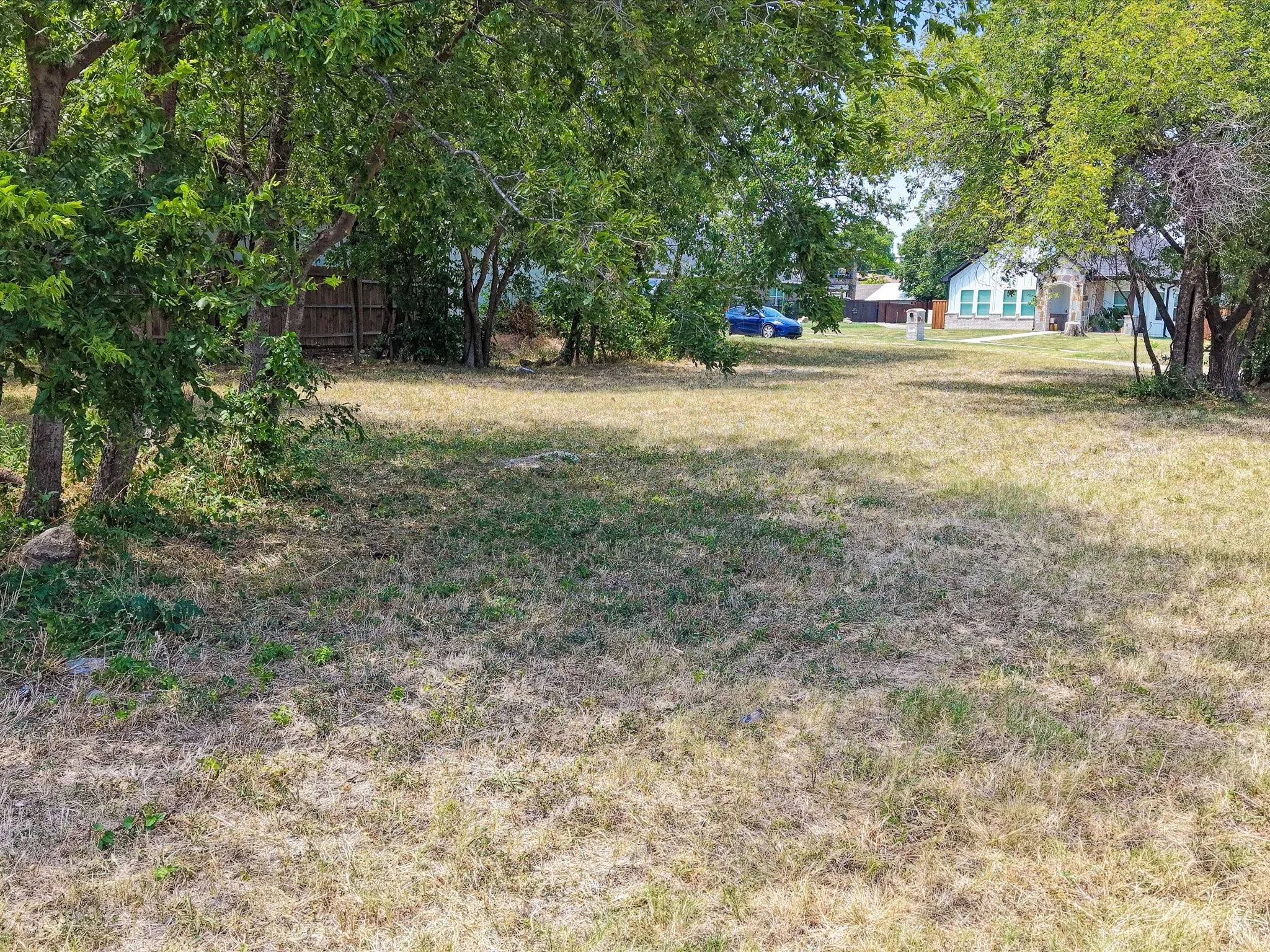 Expansive lot featuring mature trees, a partially fenced perimeter, and a distant residential structure