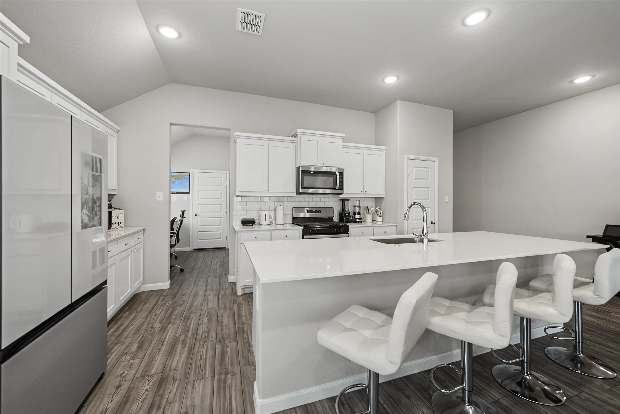 Kitchen featuring white shaker cabinetry, stainless steel appliances, a center island with a sink, quartz countertops, and wood-finish flooring