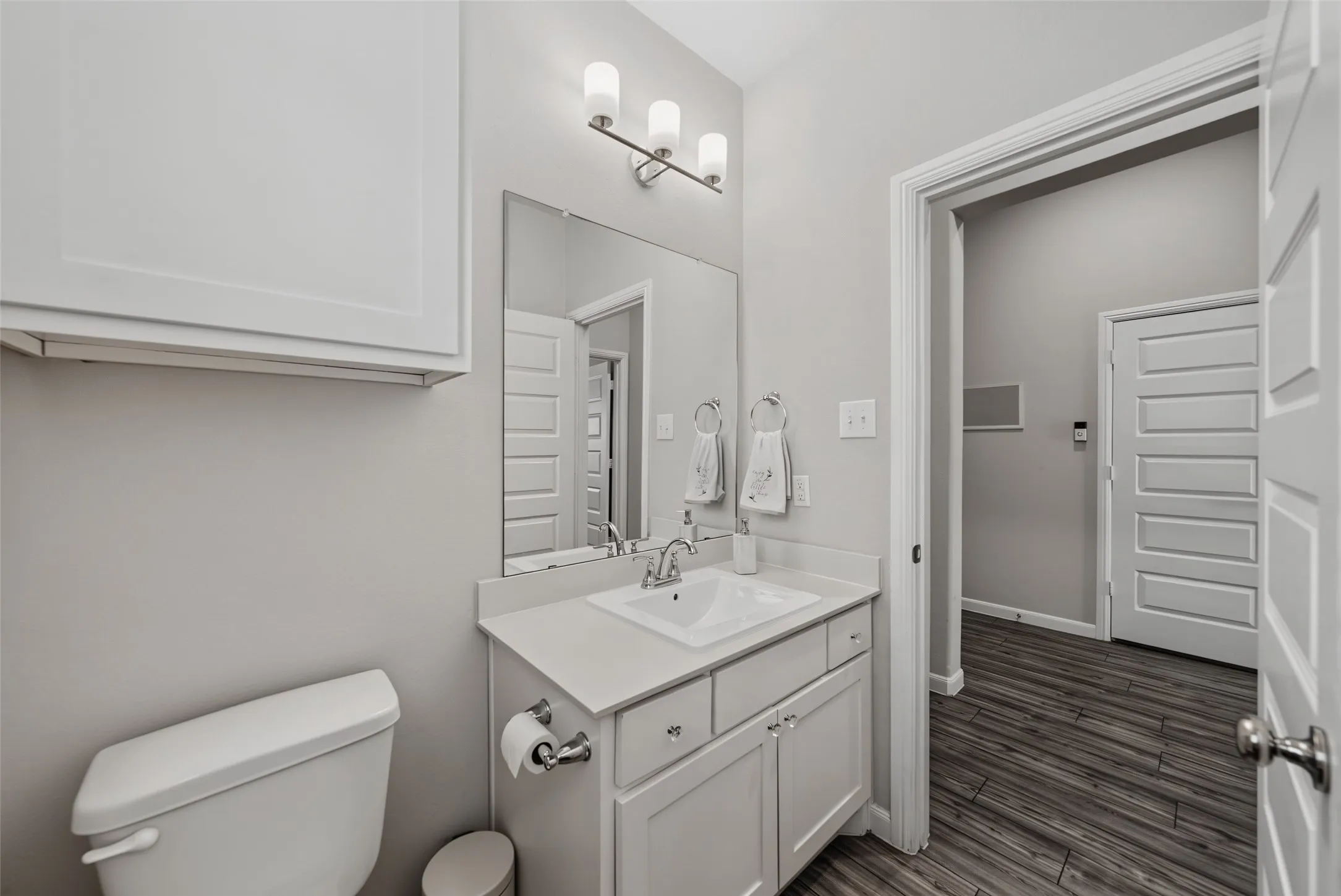 White vanity with an integrated sink, polished chrome faucet, and overhead three-light fixture
