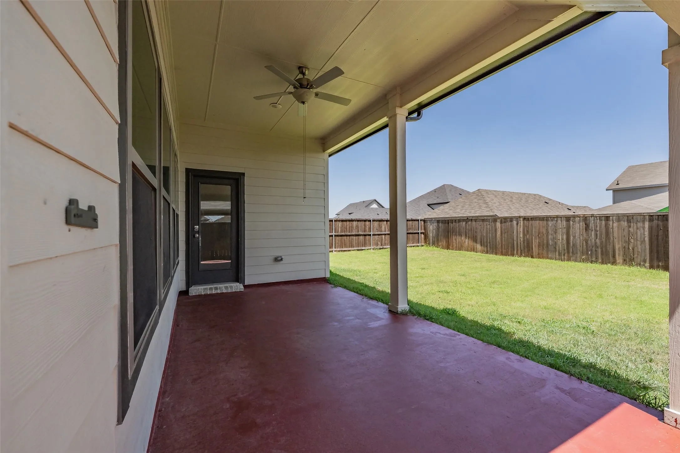 Covered patio featuring an outdoor ceiling fan, red-toned concrete flooring, and direct access to the backyard