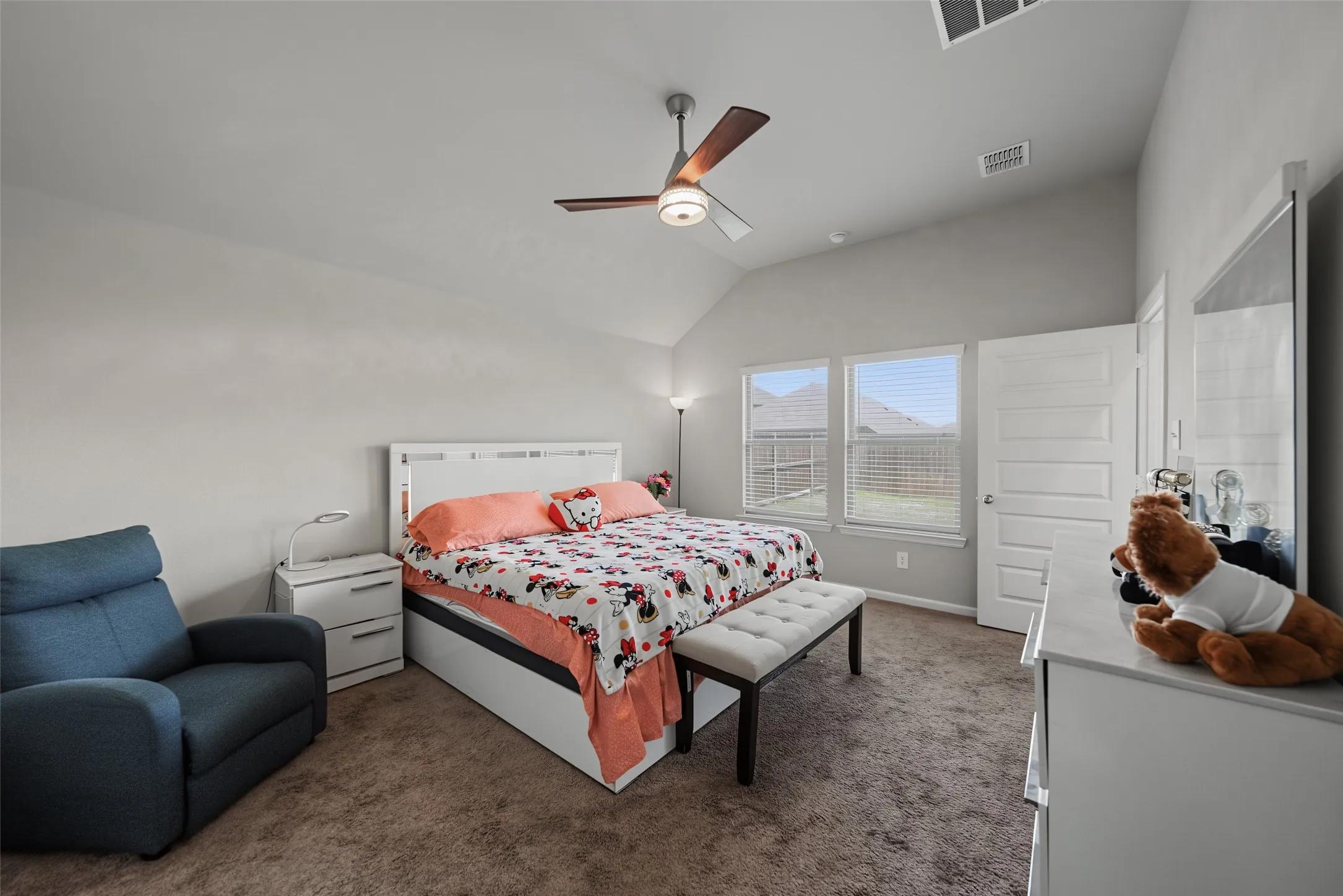 Vaulted ceiling, ceiling fan with integrated lighting, three paneled interior door, two windows, and carpet flooring