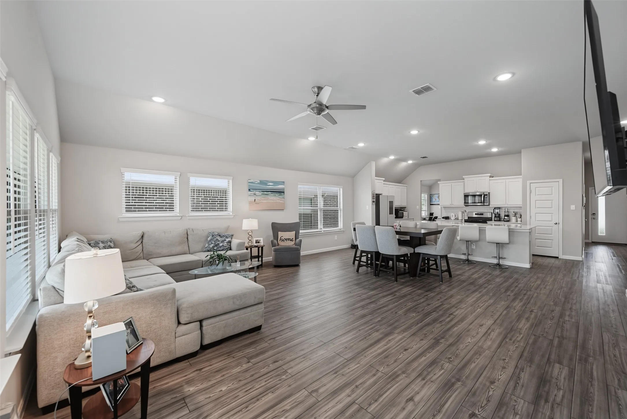 Expansive open-concept living area featuring wood-finish flooring, vaulted ceilings, and recessed lighting