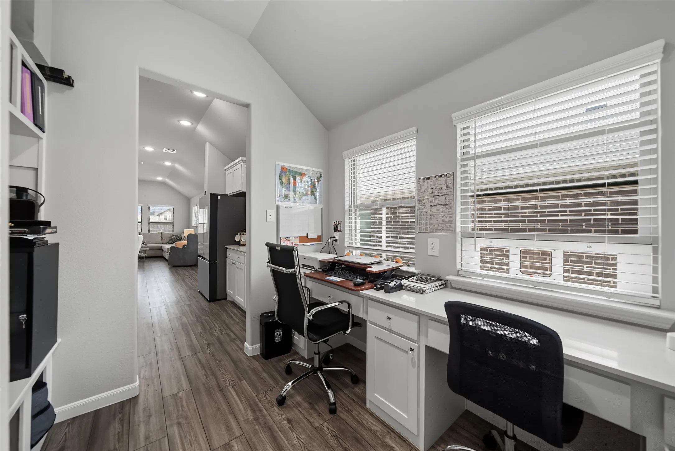Dedicated workspace featuring built-in white cabinetry, light-toned countertops, and two windows with blinds
