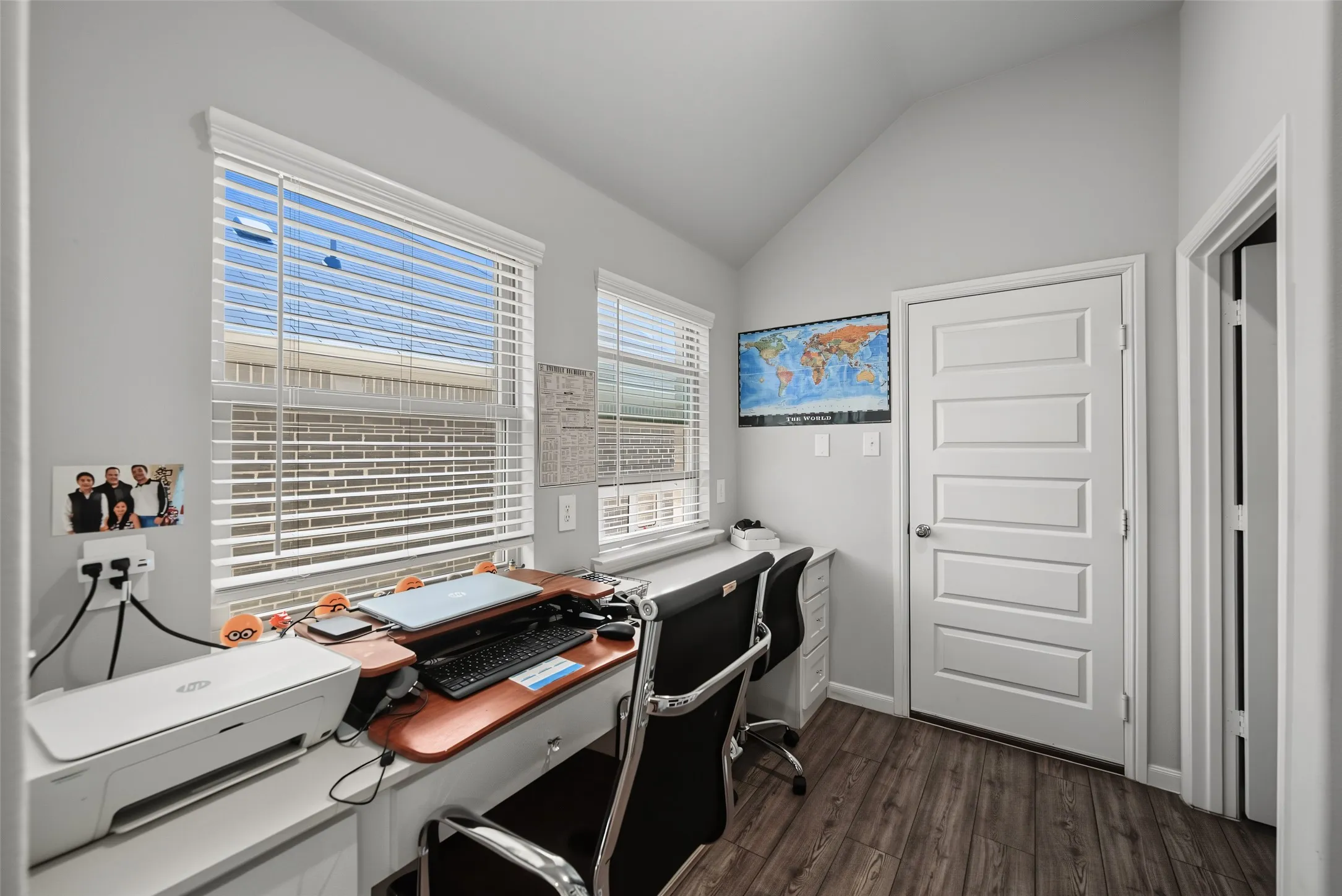 Wood-finish flooring with a multi-paneled interior door, two windows with blinds, and light gray wall paint