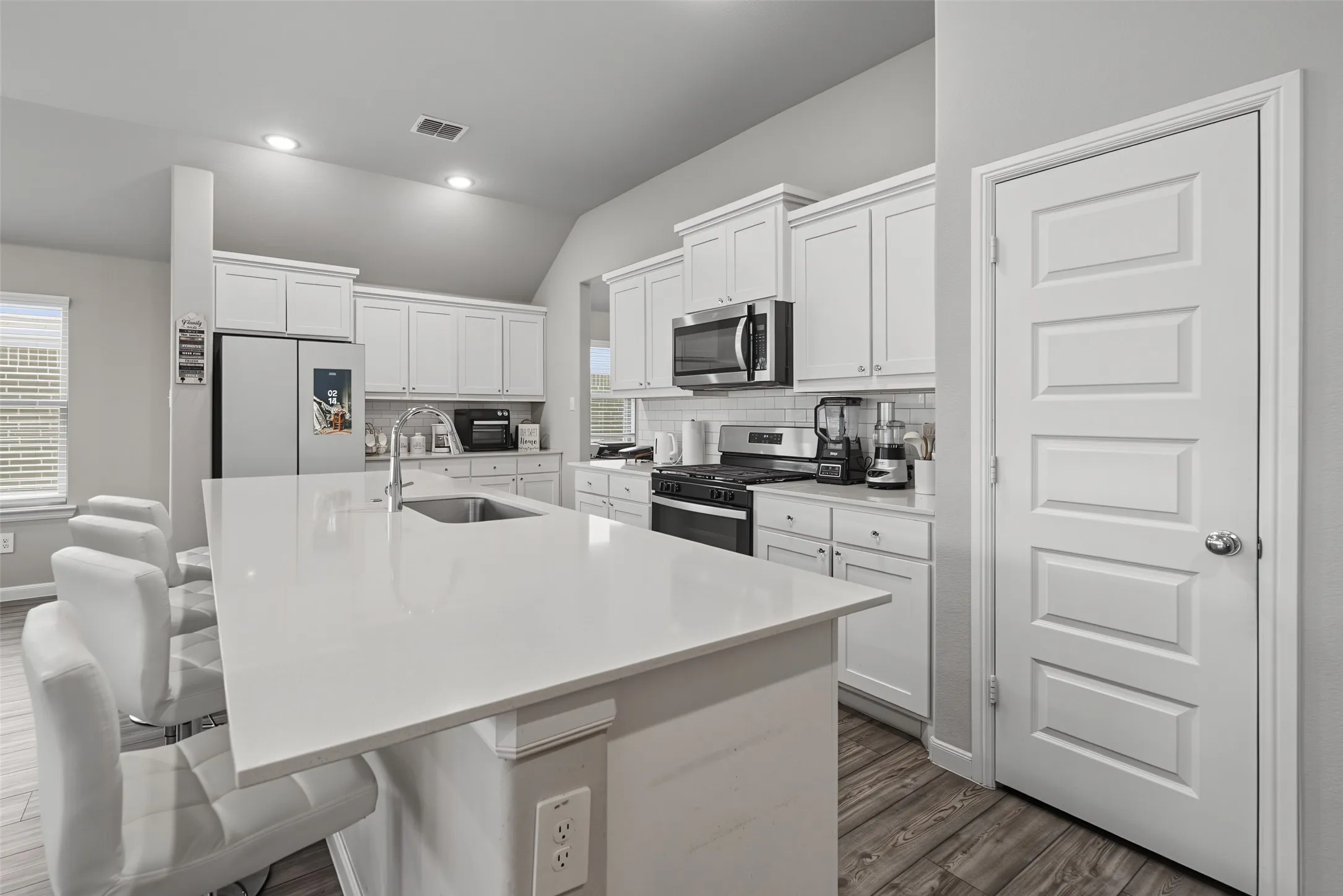 Kitchen featuring an expansive island with an undermount sink, white cabinetry, stainless steel appliances, and wood-finish flooring