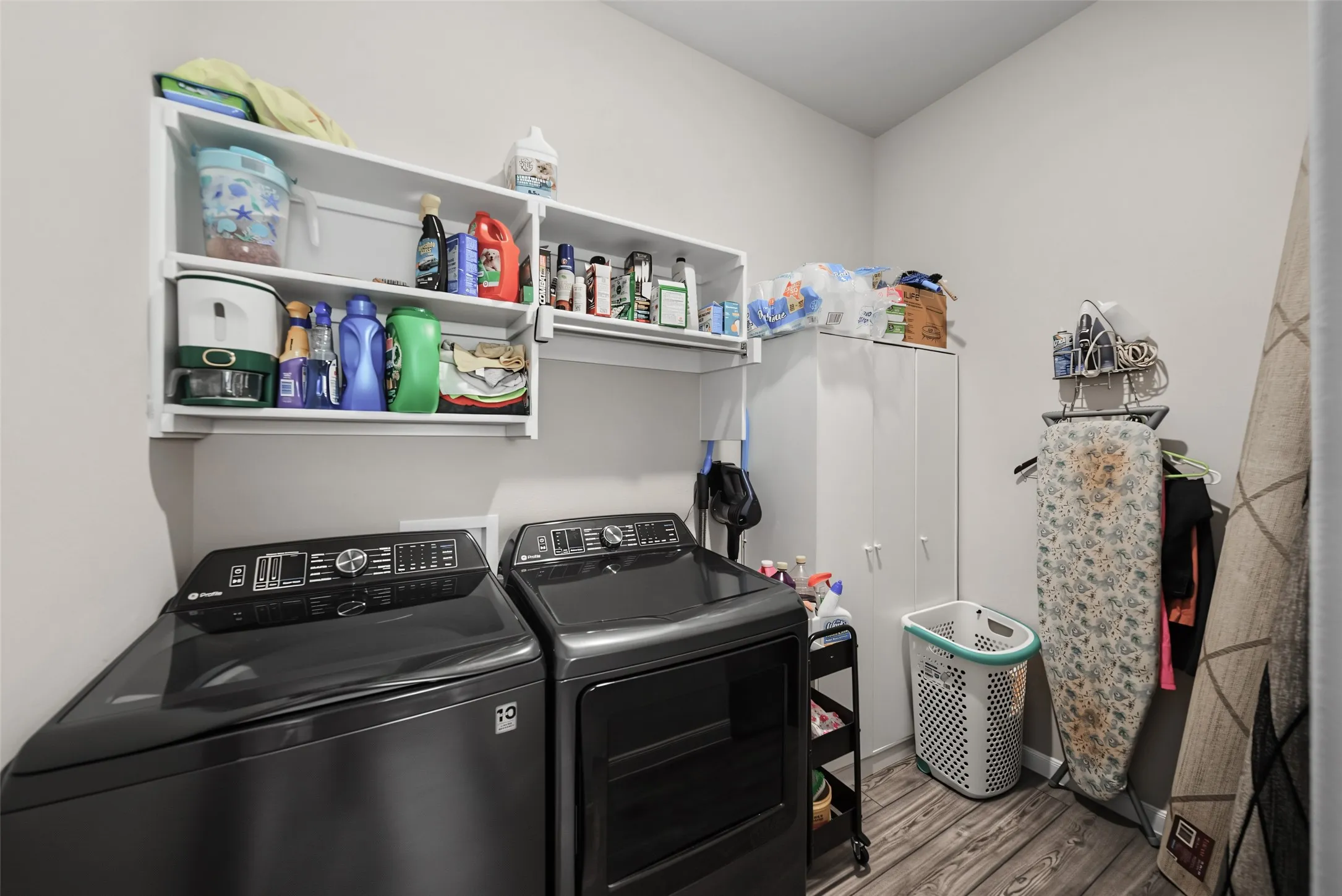 Laundry area featuring wall-mounted shelving, built-in cabinetry, and wood-finish flooring