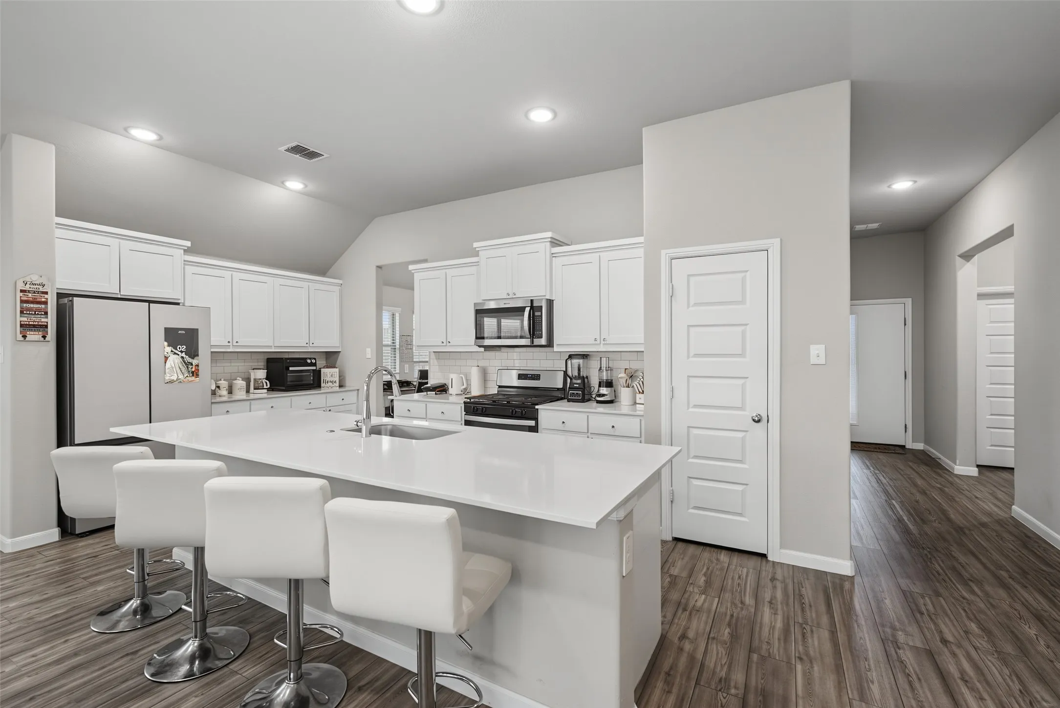 Kitchen featuring a spacious island with an integrated sink, white cabinetry, stainless steel appliances, a tile backsplash, and wood-finish flooring