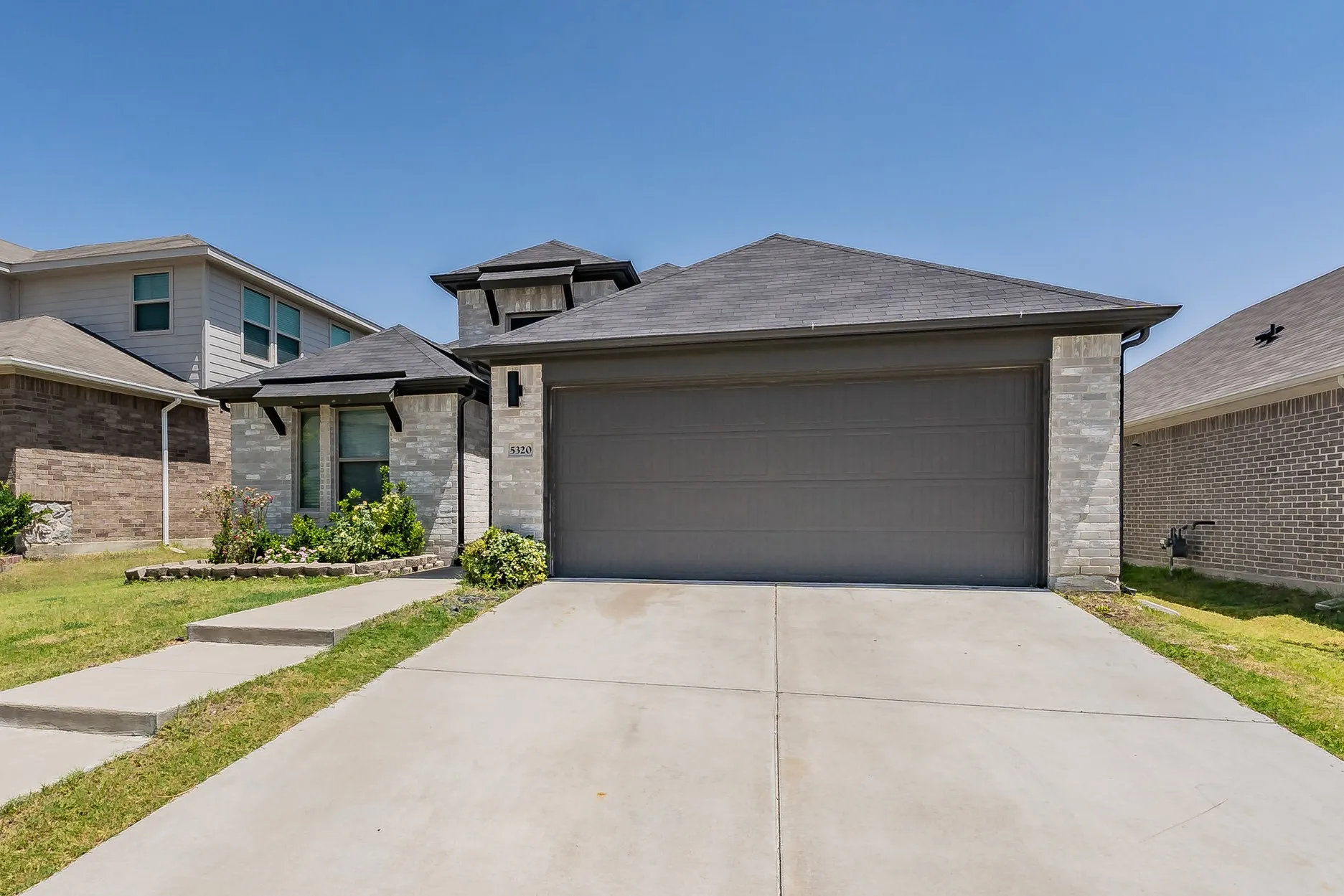 Stone facade exterior with a two-car garage, concrete driveway, and front landscaping