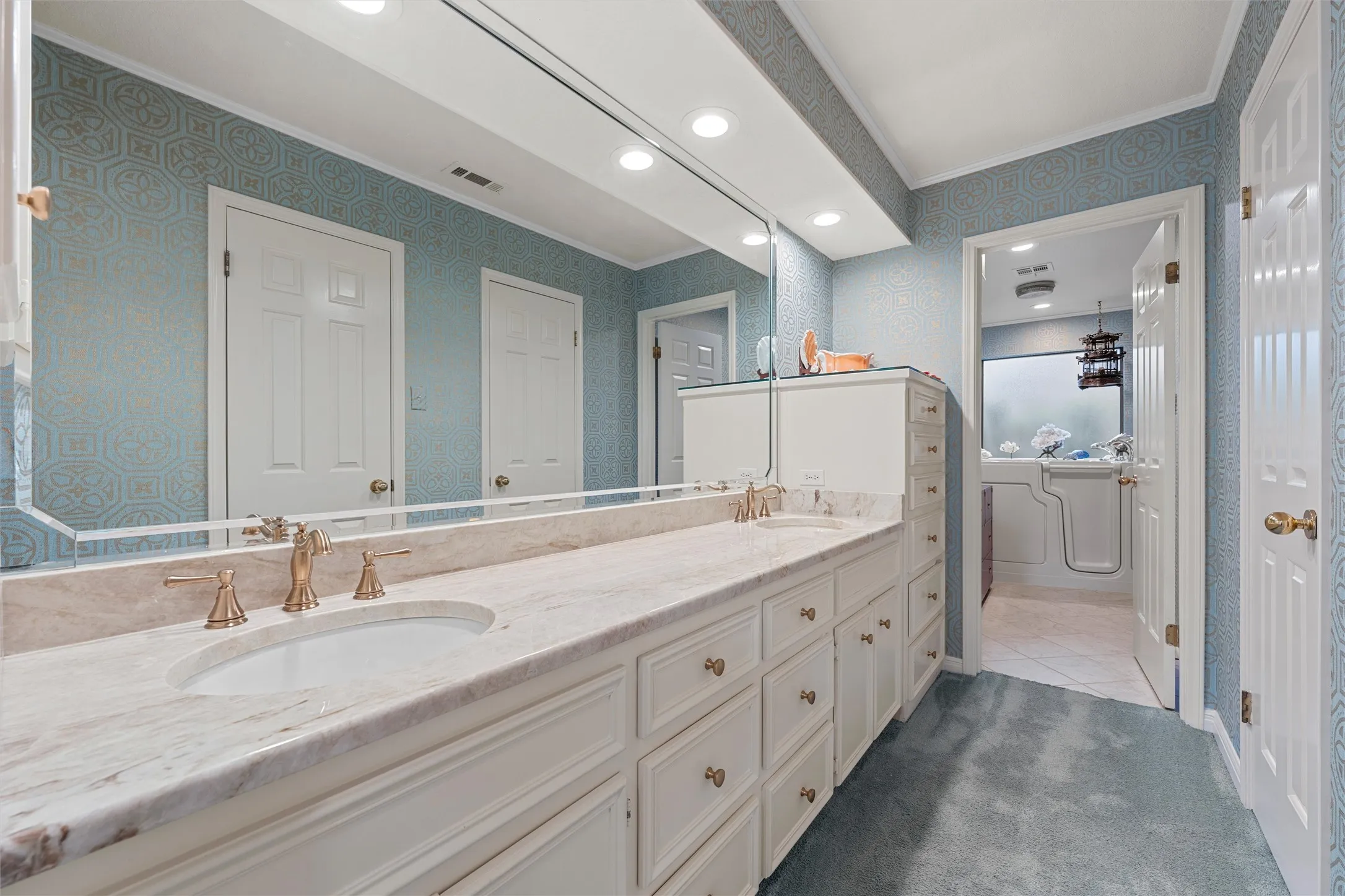 Bathroom featuring a dual vanity with a light-toned countertop, white cabinetry, and gold-finish fixtures