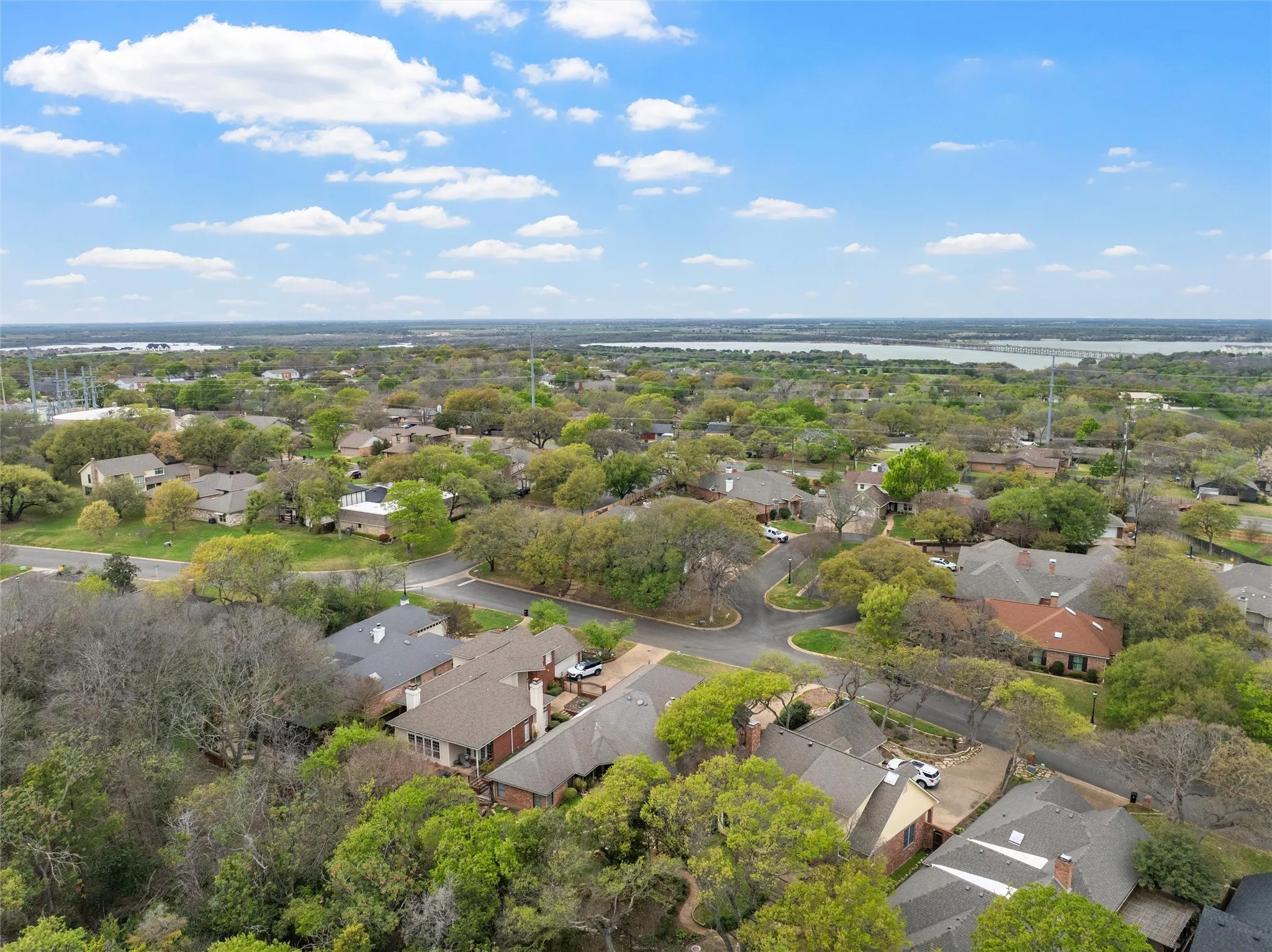 Aerial view of a residential area featuring mature trees and a distant body of water
