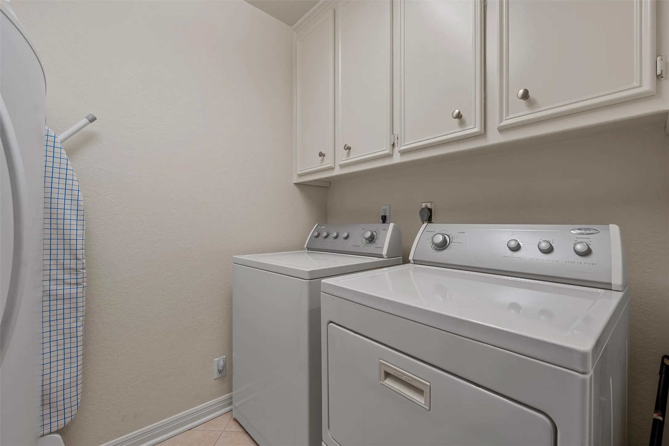 Dedicated laundry area featuring white upper cabinetry with brushed nickel hardware, light-toned walls, and white baseboards