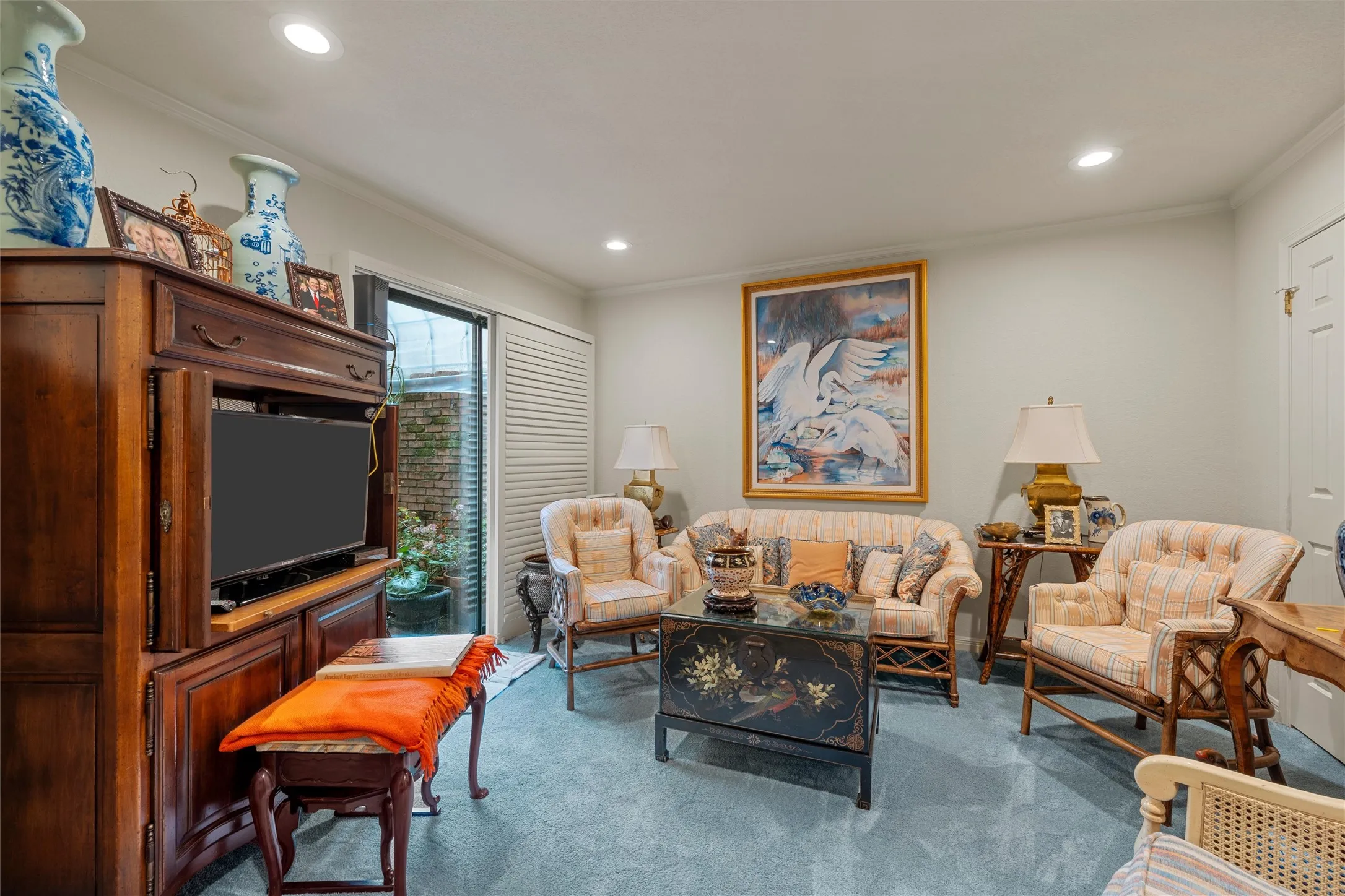 Living area featuring light blue carpet, a large wood entertainment cabinet, recessed lighting, and a sliding glass door to an exterior space