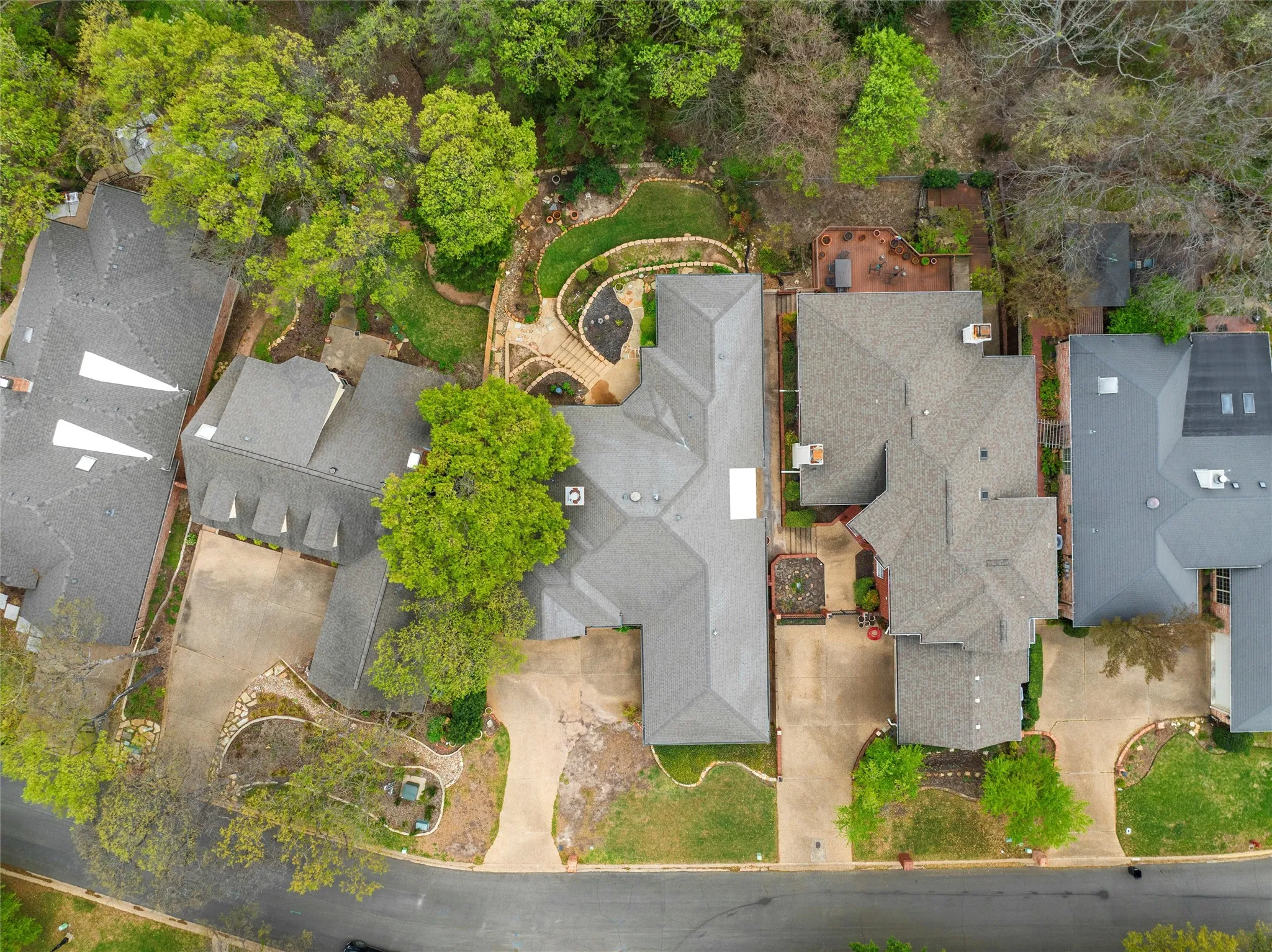 Aerial view showcasing a multi-unit residential property with distinctive architectural design, featuring multiple pitched roofs with gray asphalt shingles, concrete driveways, and mature landscaping throughout the grounds