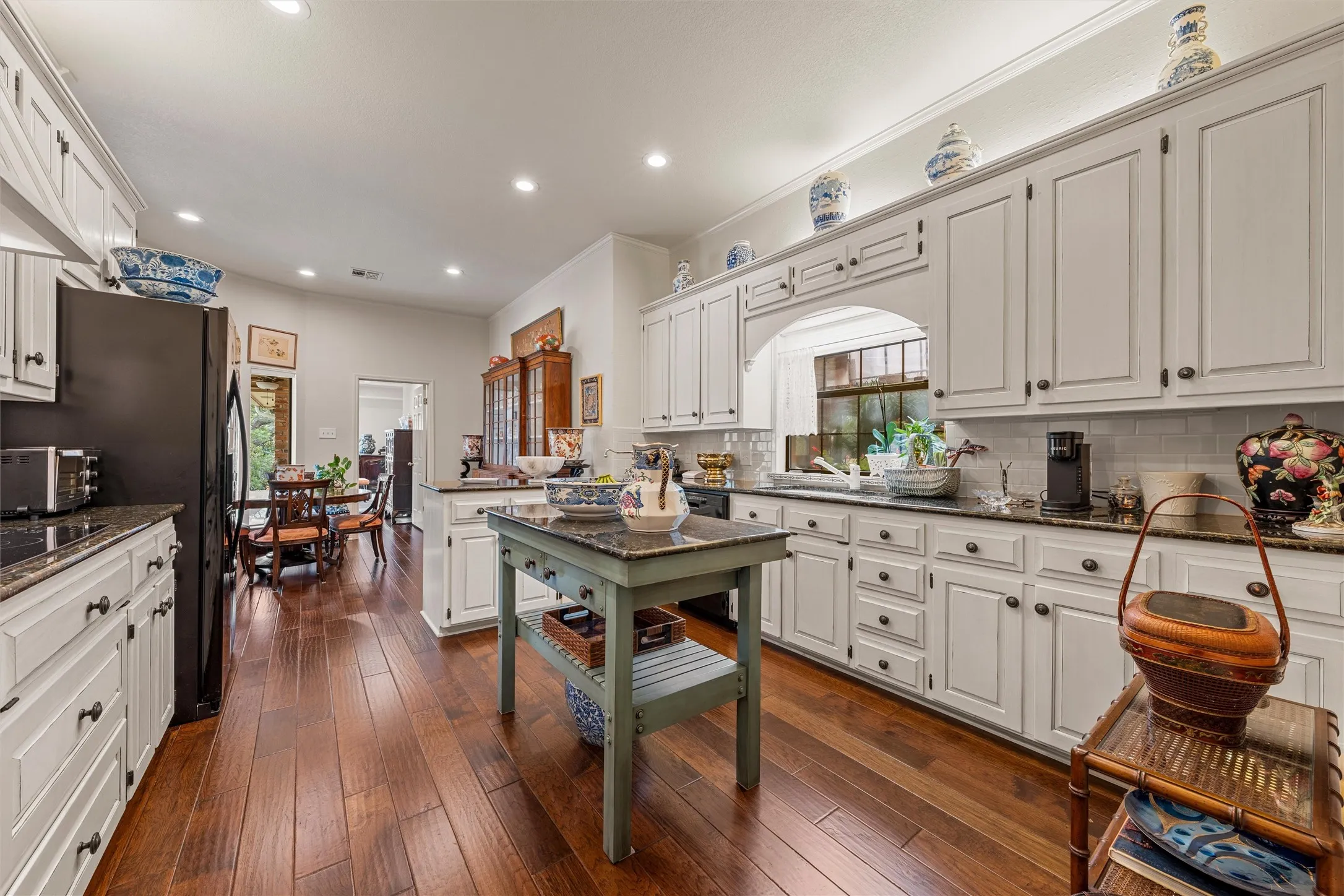 Spacious kitchen featuring extensive white cabinetry, dark stone countertops, wood-finish flooring, and recessed lighting