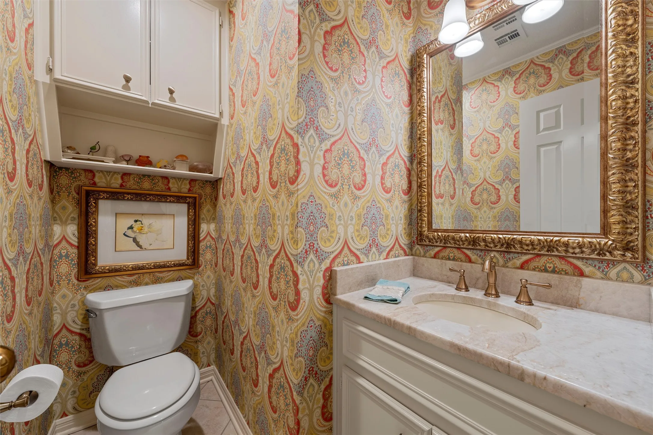 Vanity with an integrated sink and light-toned countertop, featuring a decorative gold-framed mirror