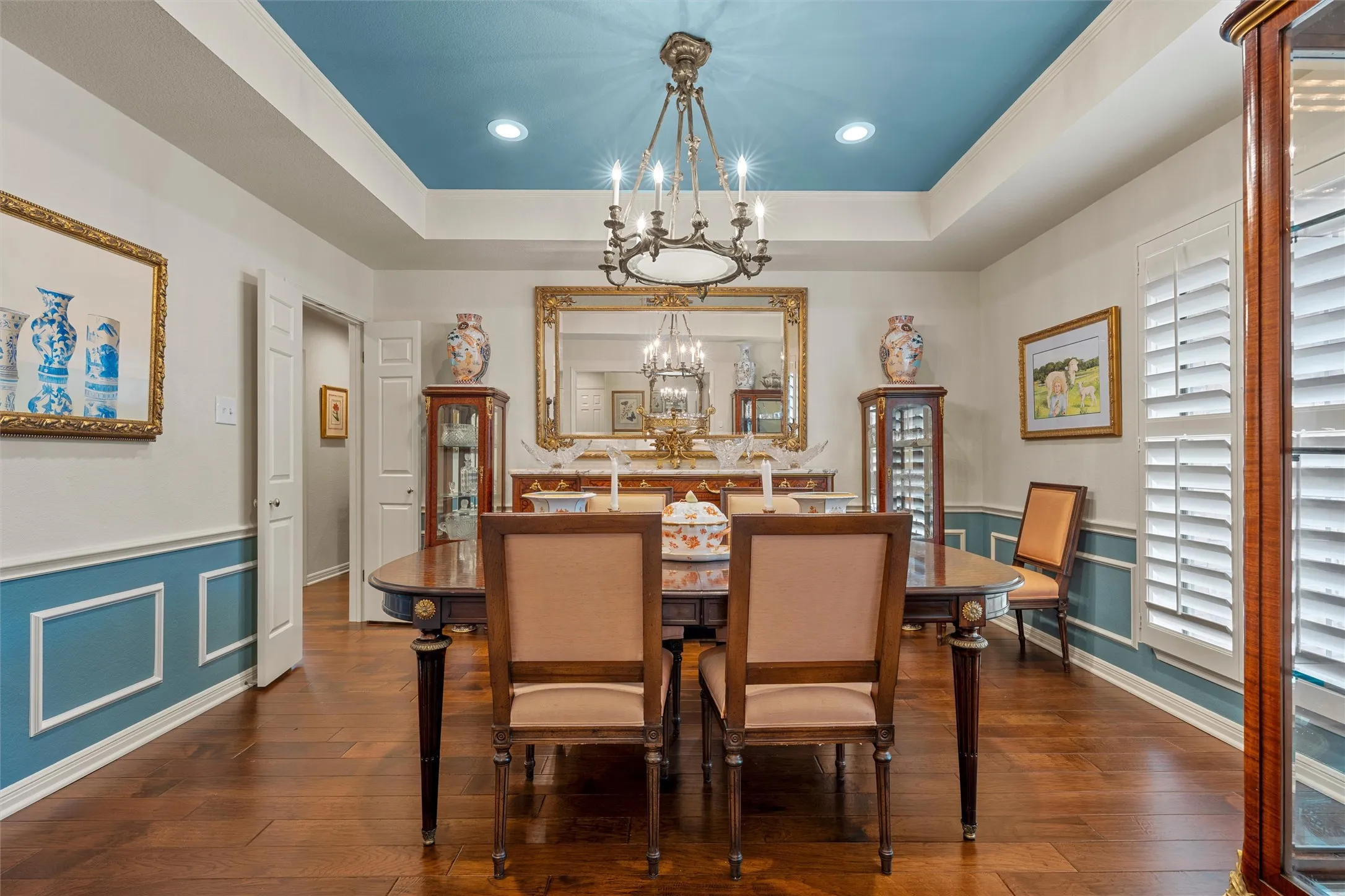 Formal dining room featuring wood-finish flooring, a tray ceiling with recessed lighting and chandelier, and wainscoting
