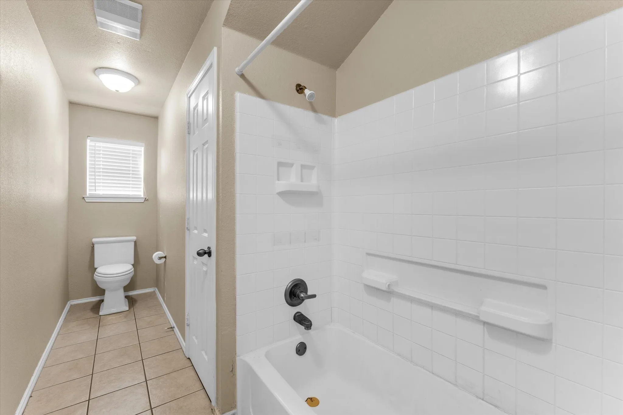 White tiled tub and shower combination with dark bronze fixtures