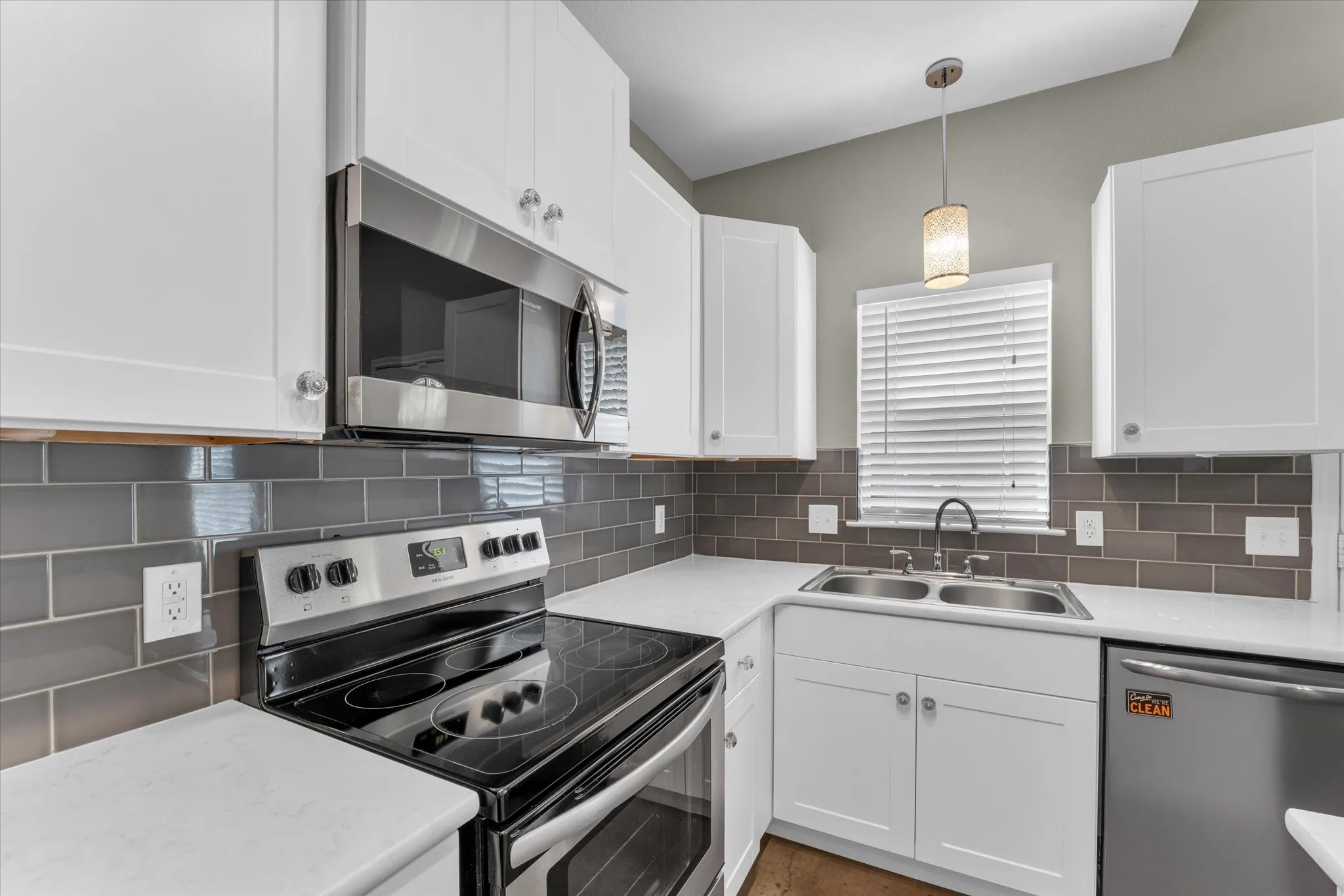 Modern kitchen featuring white cabinetry, stainless steel appliances, a grey subway tile backsplash, white countertops, and a dual basin sink with a gooseneck faucet