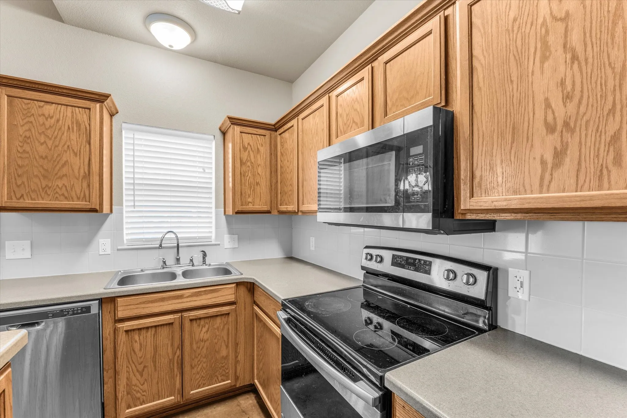 Kitchen featuring wood cabinetry, stainless steel appliances including a built-in microwave and dishwasher, a dual basin stainless steel sink, and light-toned countertops