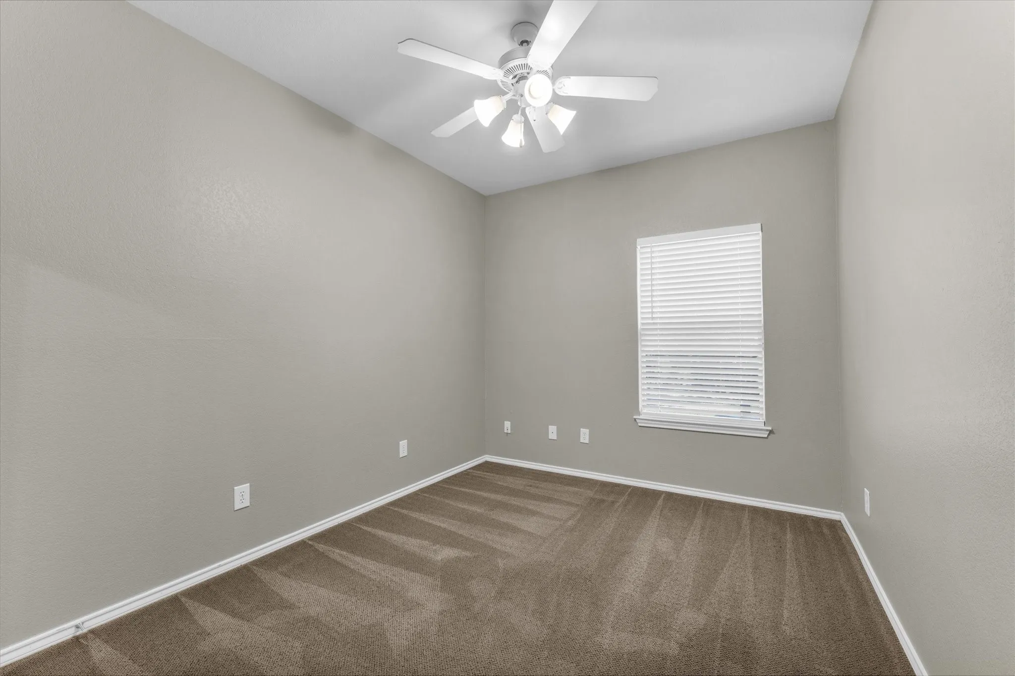 Carpeted room featuring a white ceiling fan with integrated lighting, a single window with blinds, and light gray painted walls