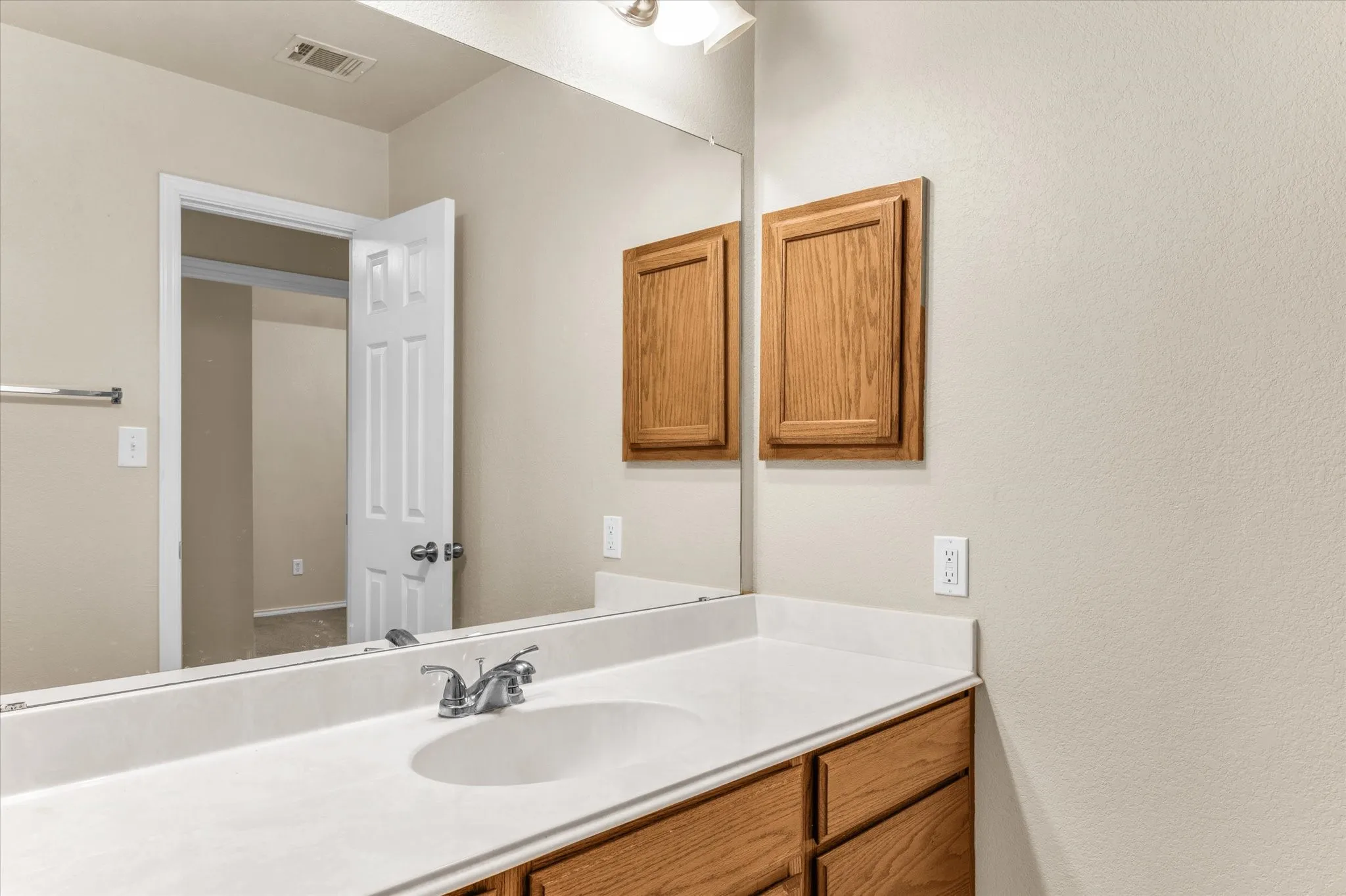 Bathroom vanity featuring a white countertop with an integrated sink, polished chrome faucet, and wood-finish cabinetry