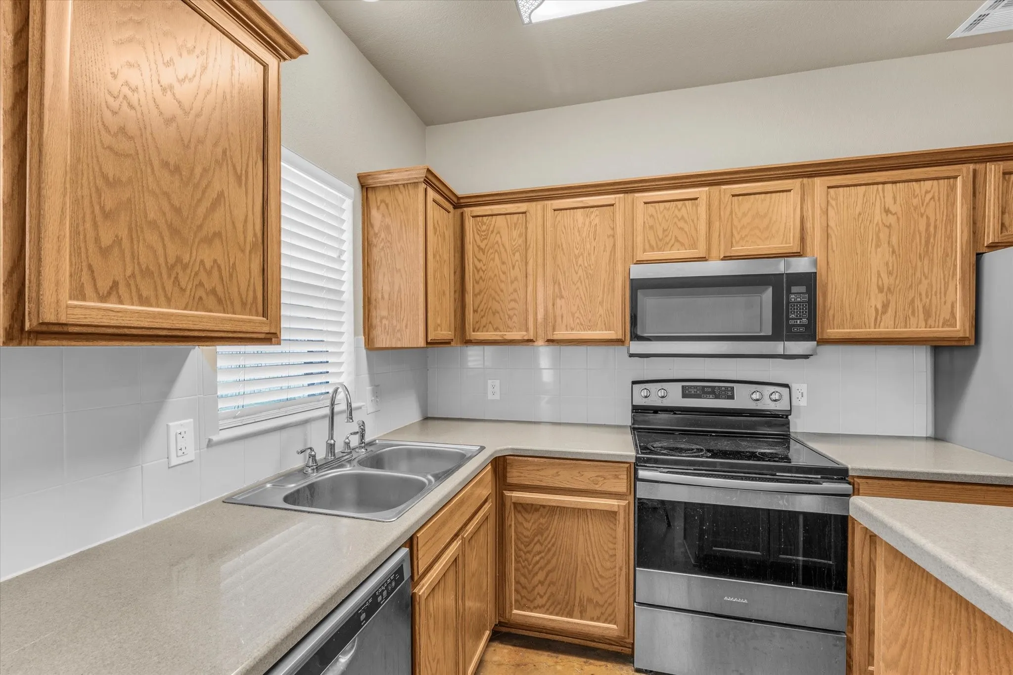 Kitchen with wood-finish cabinetry, light-toned countertops, and a white tile backsplash